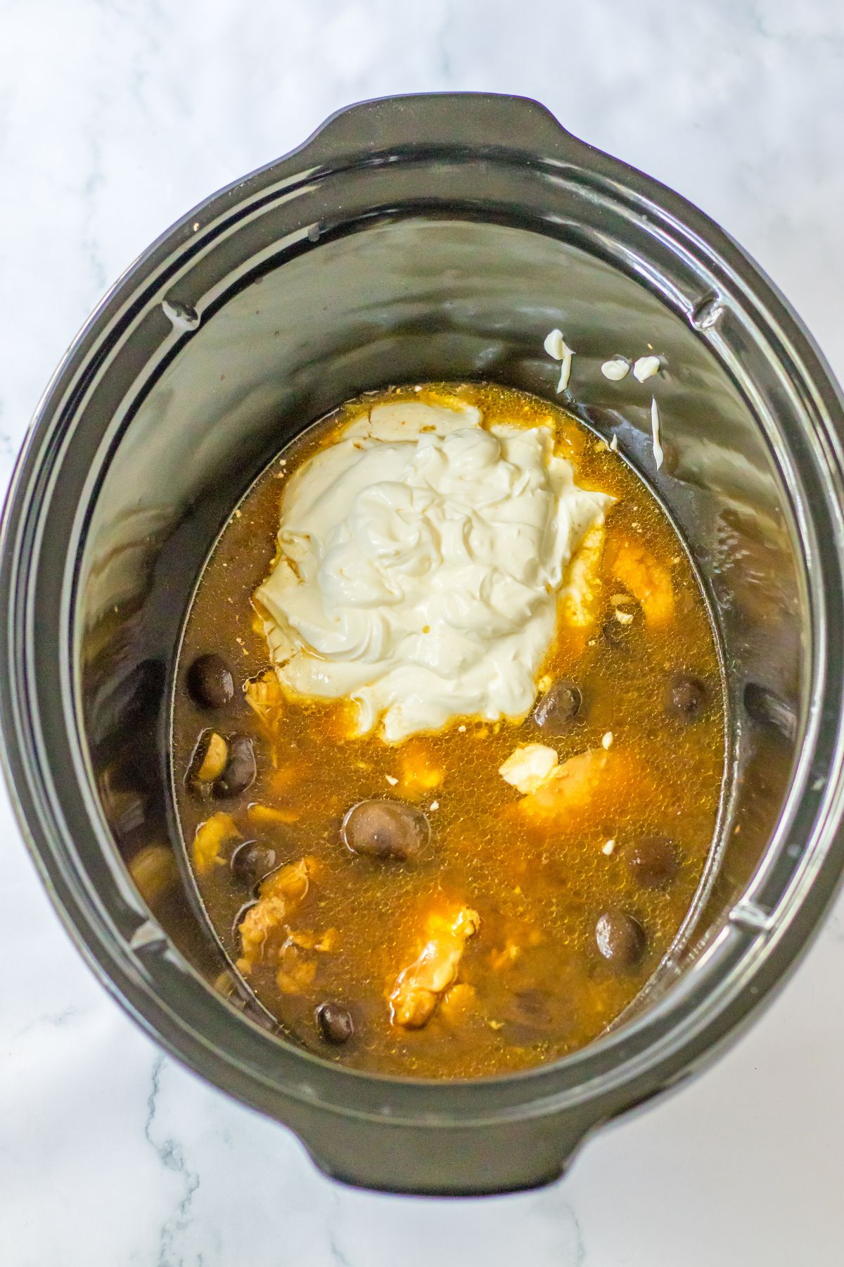 sour cream and cream cheese being stirred into a slow cooker.