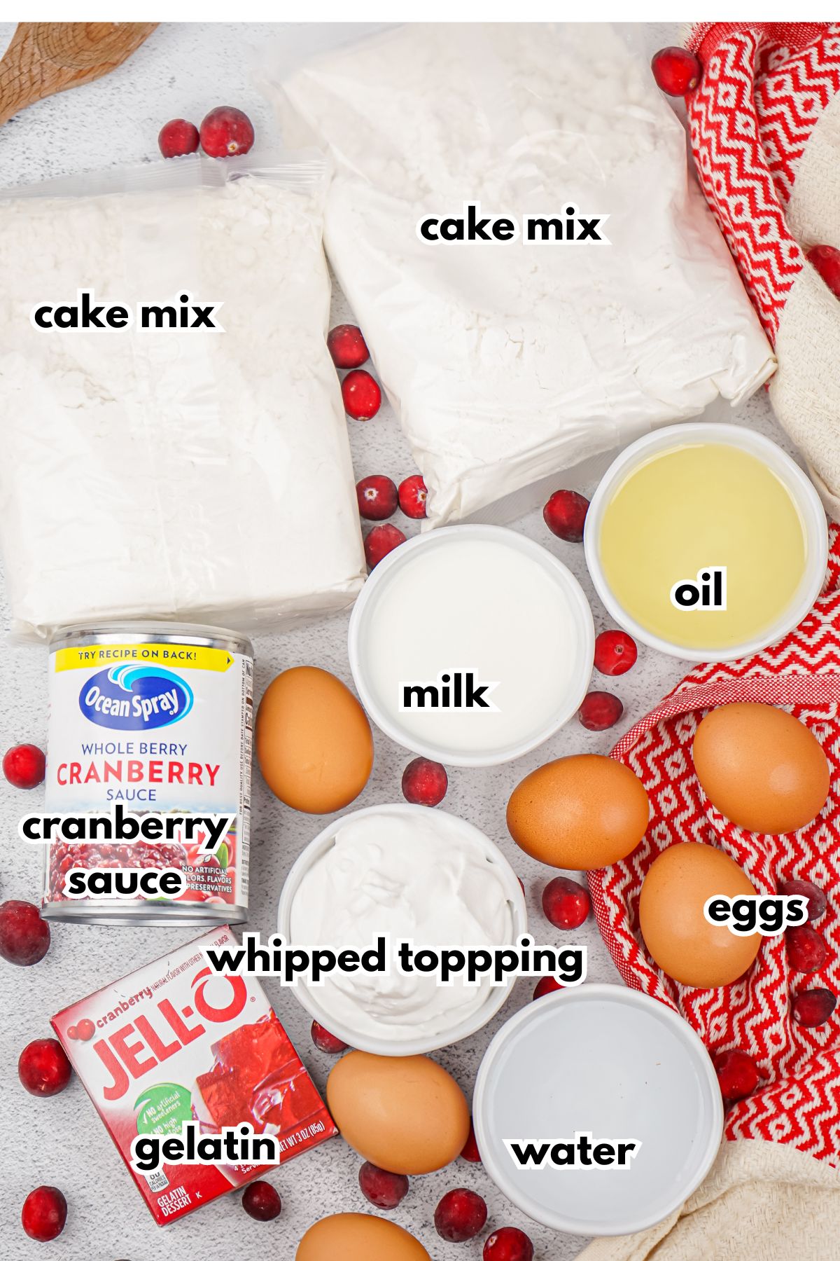 bags of cake mix, can of cranberry sauce, box of jello, and bowls of whipped topping, milk, oil, water, and eggs on a counter.