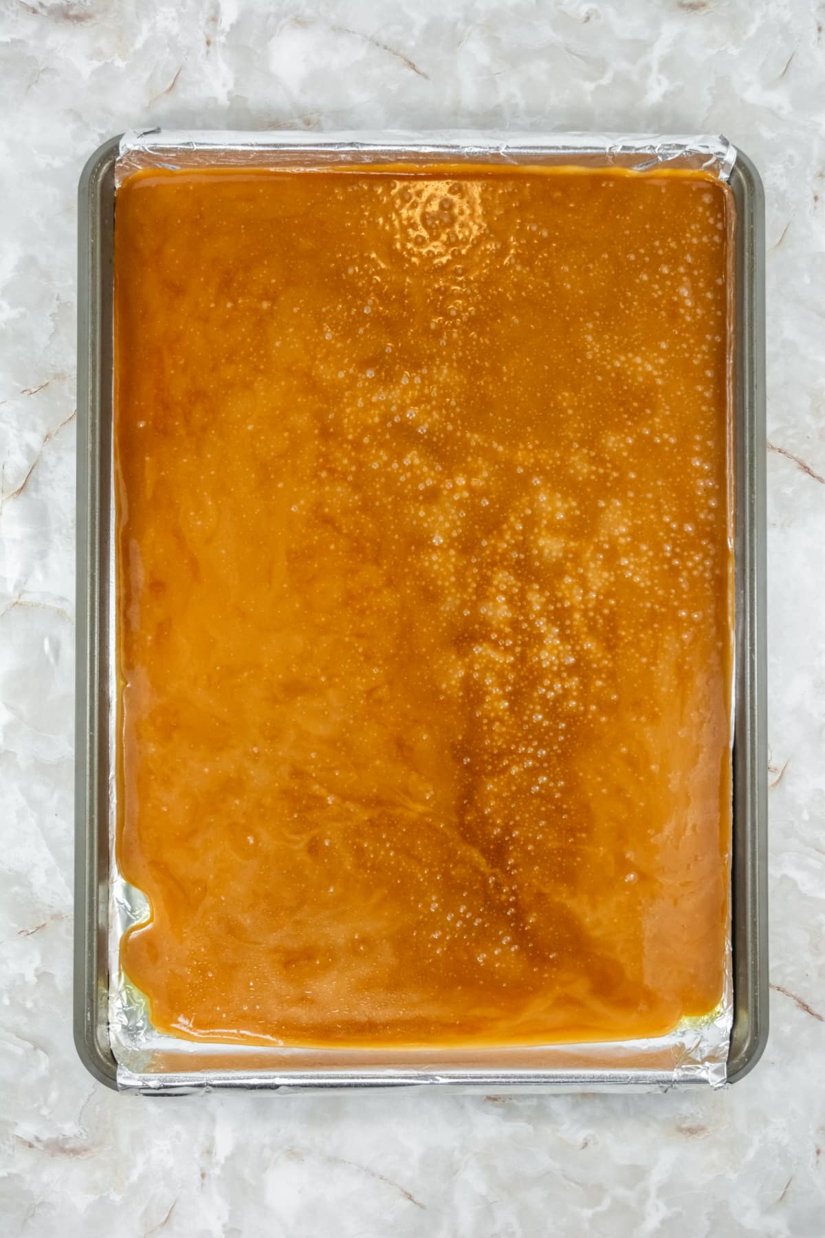 toffee being poured onto a foil lined baking sheet.