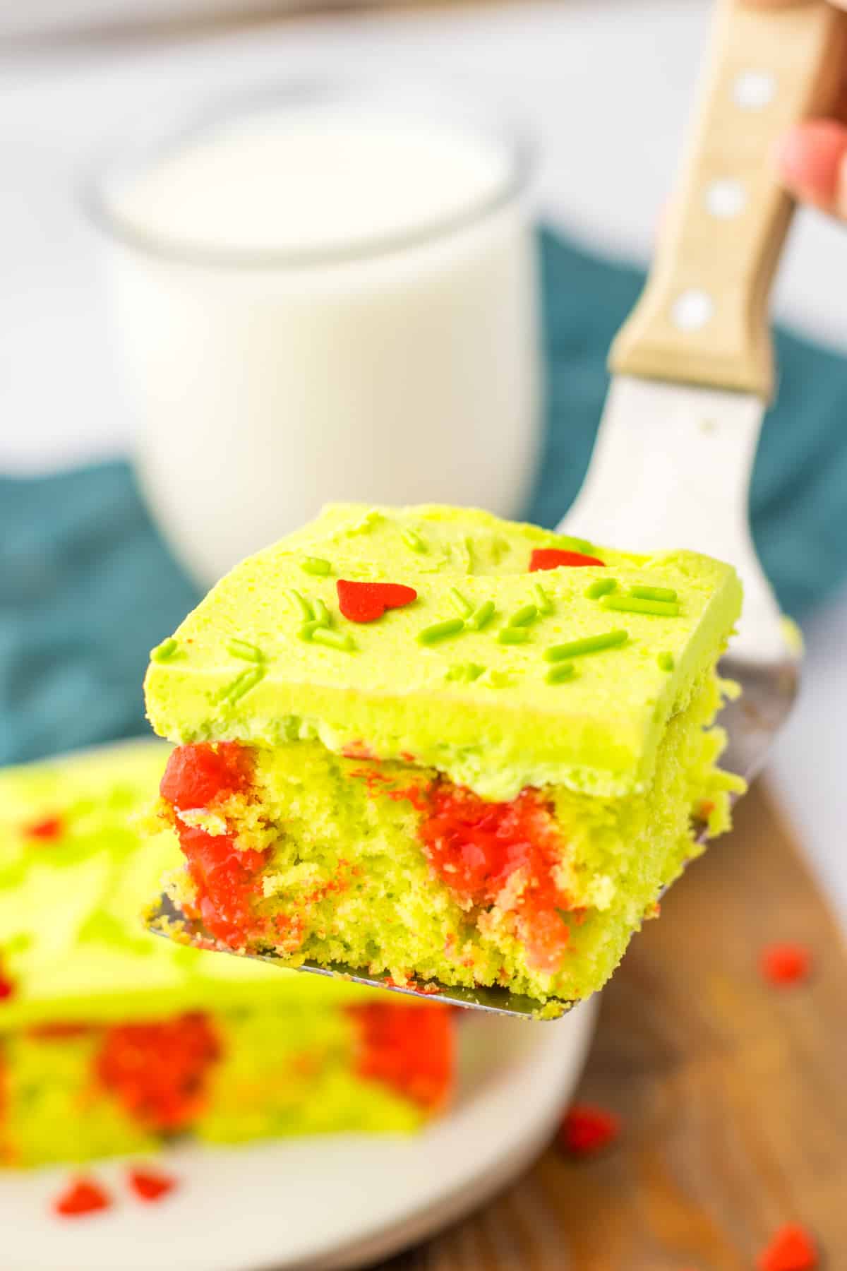 slice of grinch poke cake held in the air on a metal spatula.