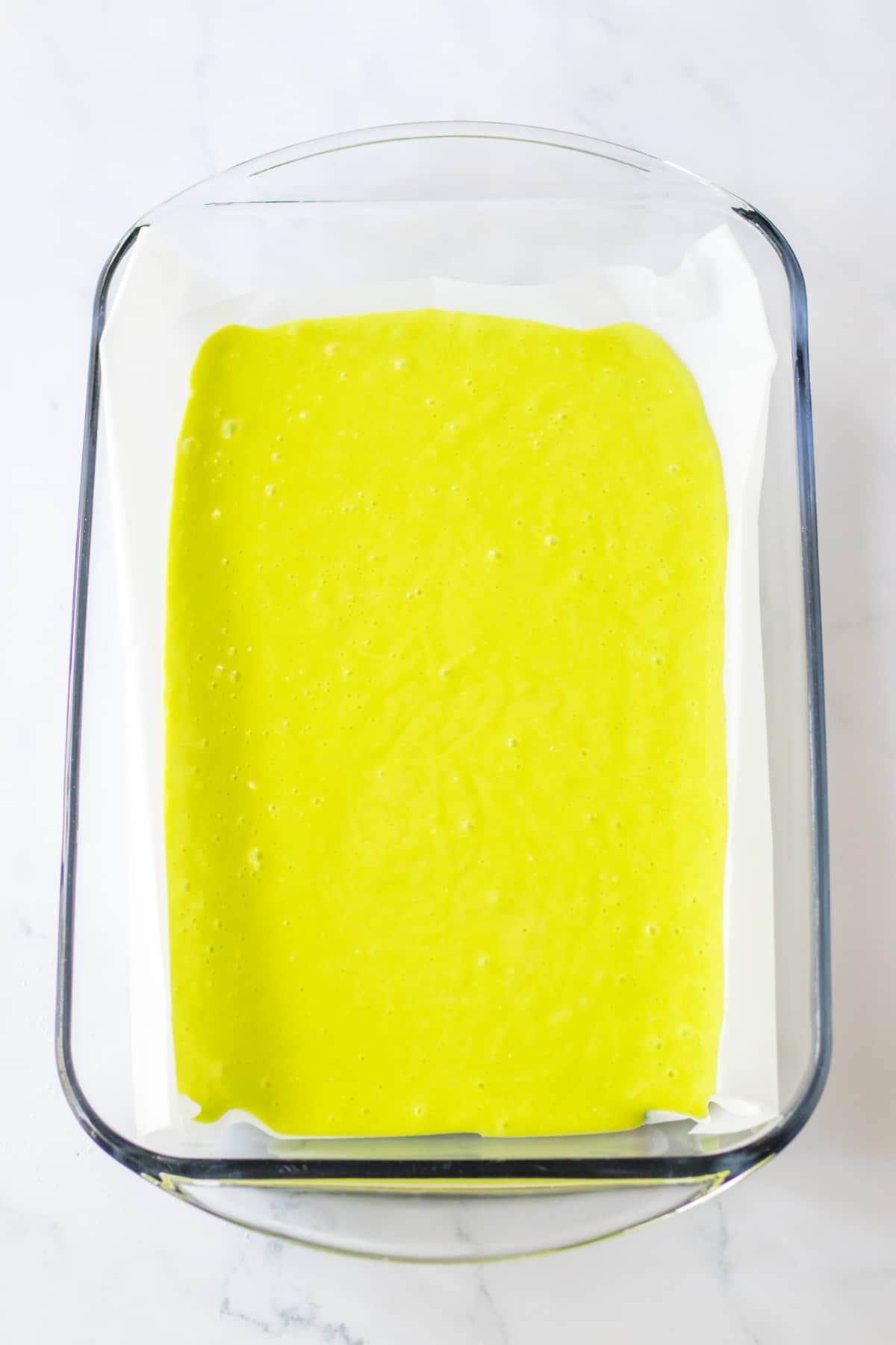 green cake batter in a parchment lined baking dish.