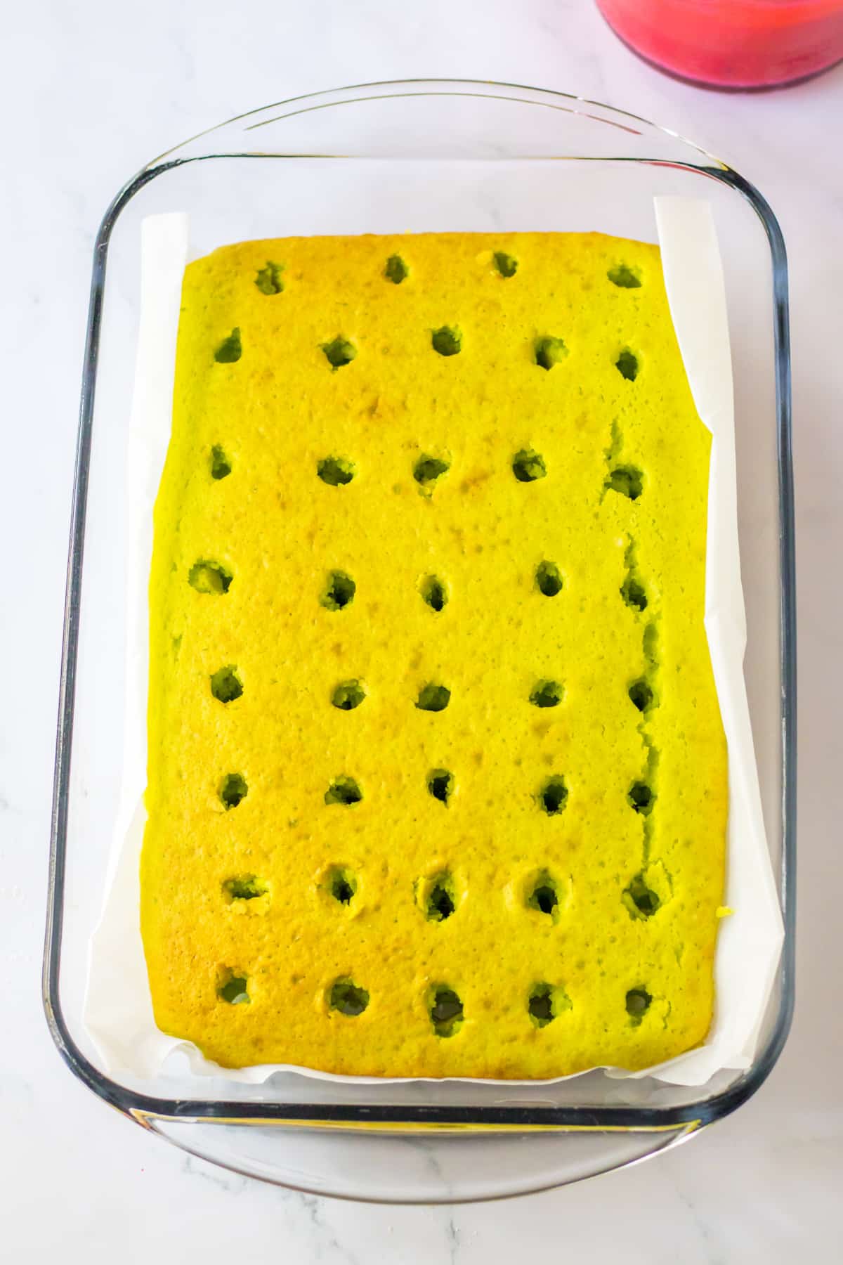 holes being added to a baked cake in a glass baking dish.