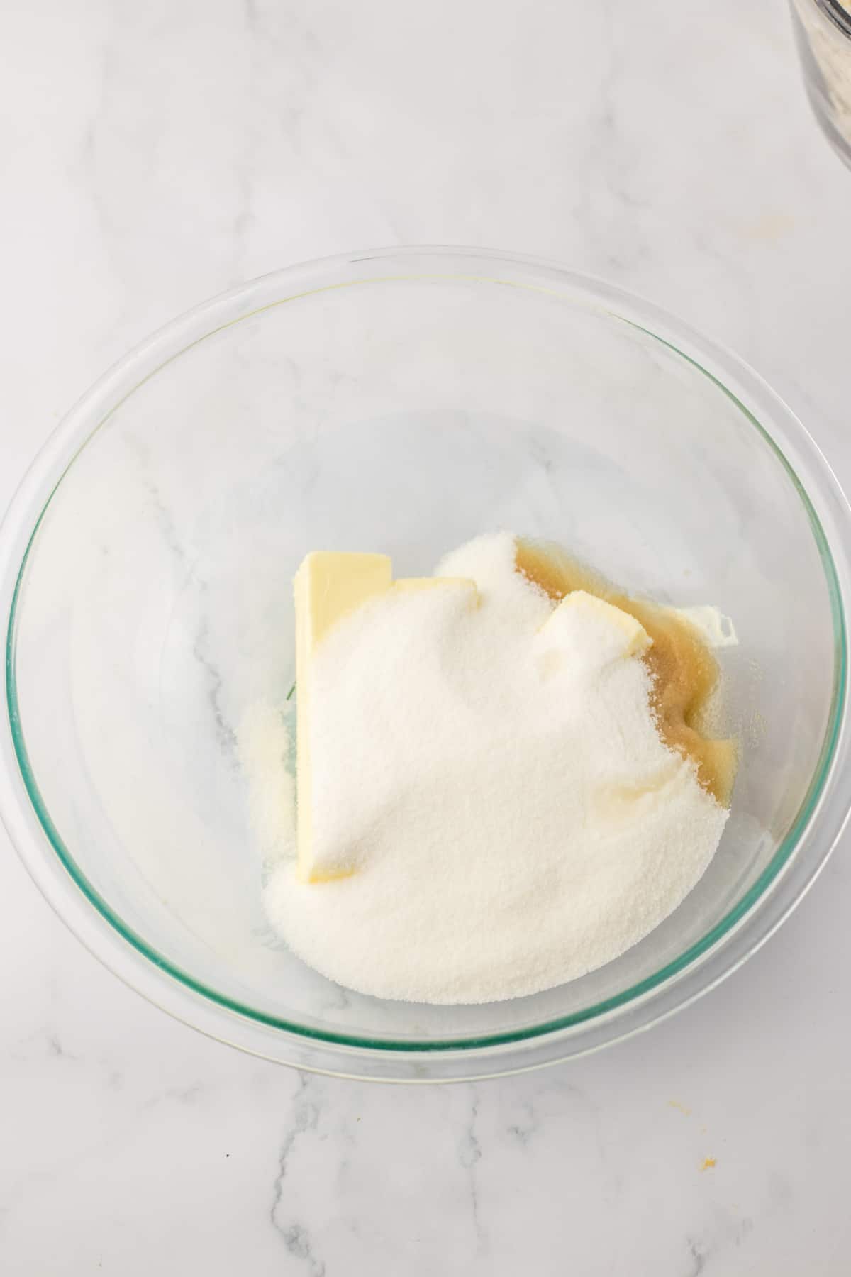 butter, sugar, and vanilla being mixed in a glass mixing bowl.