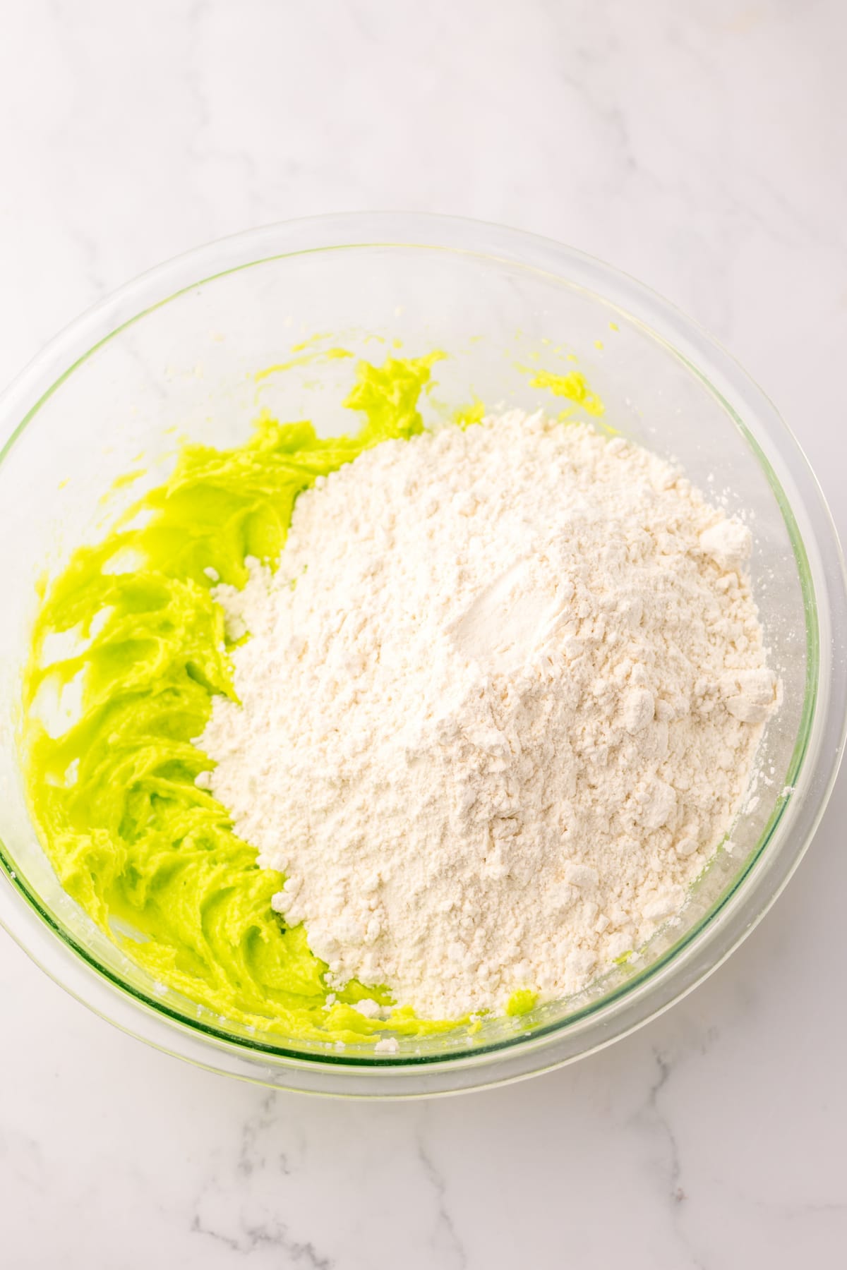 flour being mixed into the cookie dough in a glass bowl.