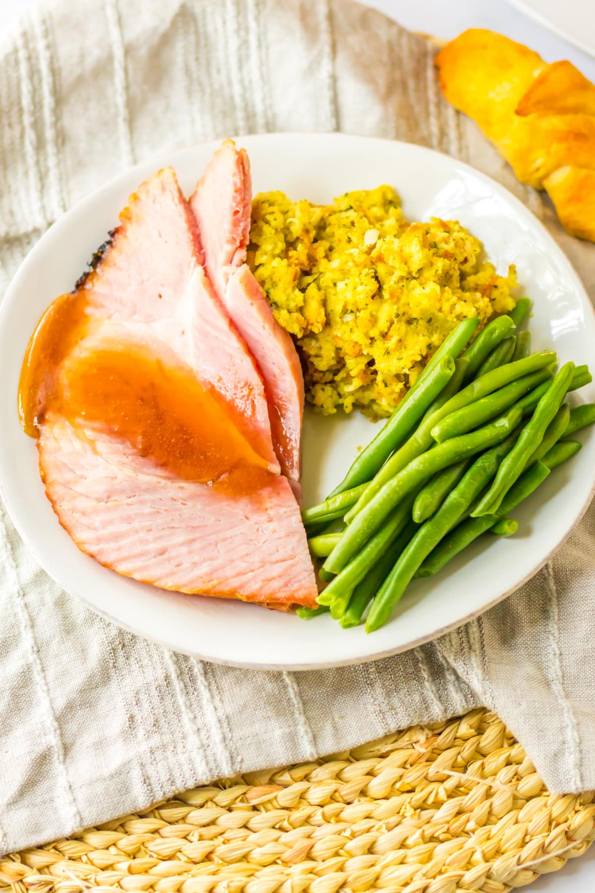 plate with slices of honey glazed ham, stuffing and green beans on a dinner plate.