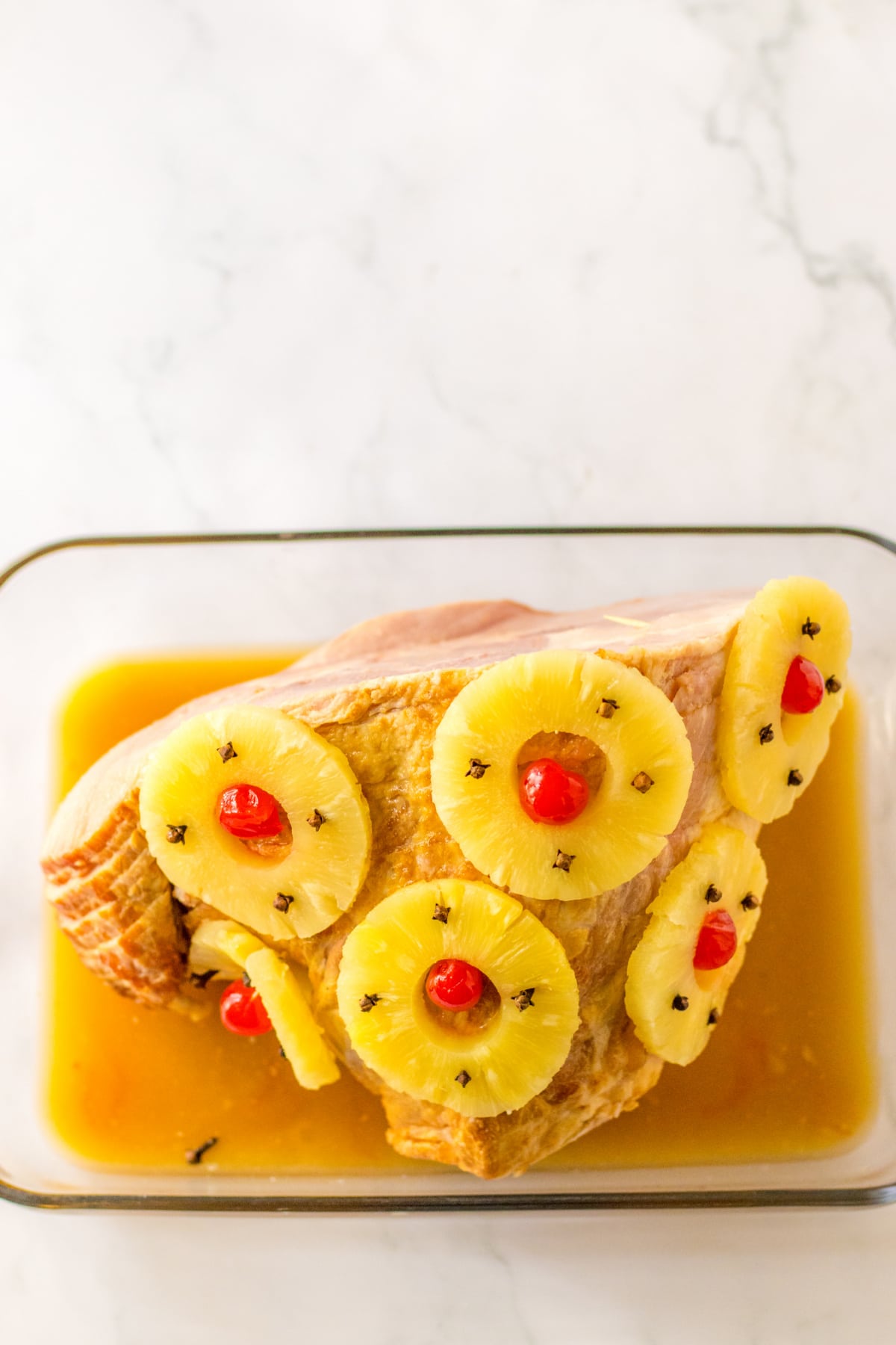 spiral ham topped with cherries and pineapple rings in a baking dish.