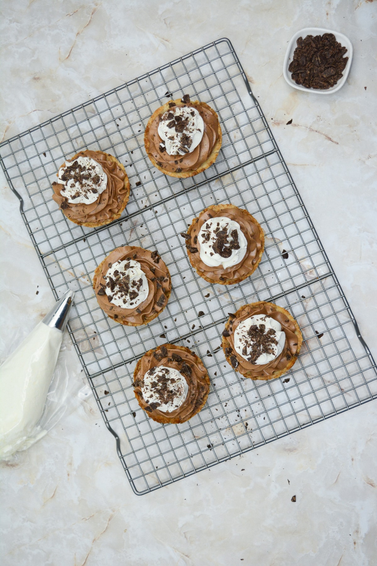 mini pies being topped with whipped cream and chocolate shavings.