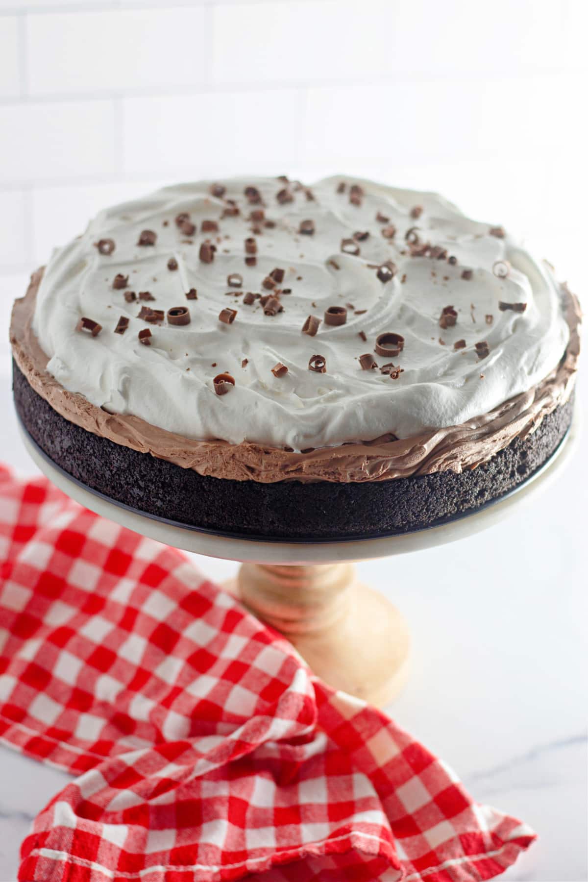 uncut no bake chocolate cheesecake with oreo crust on a cake stand.