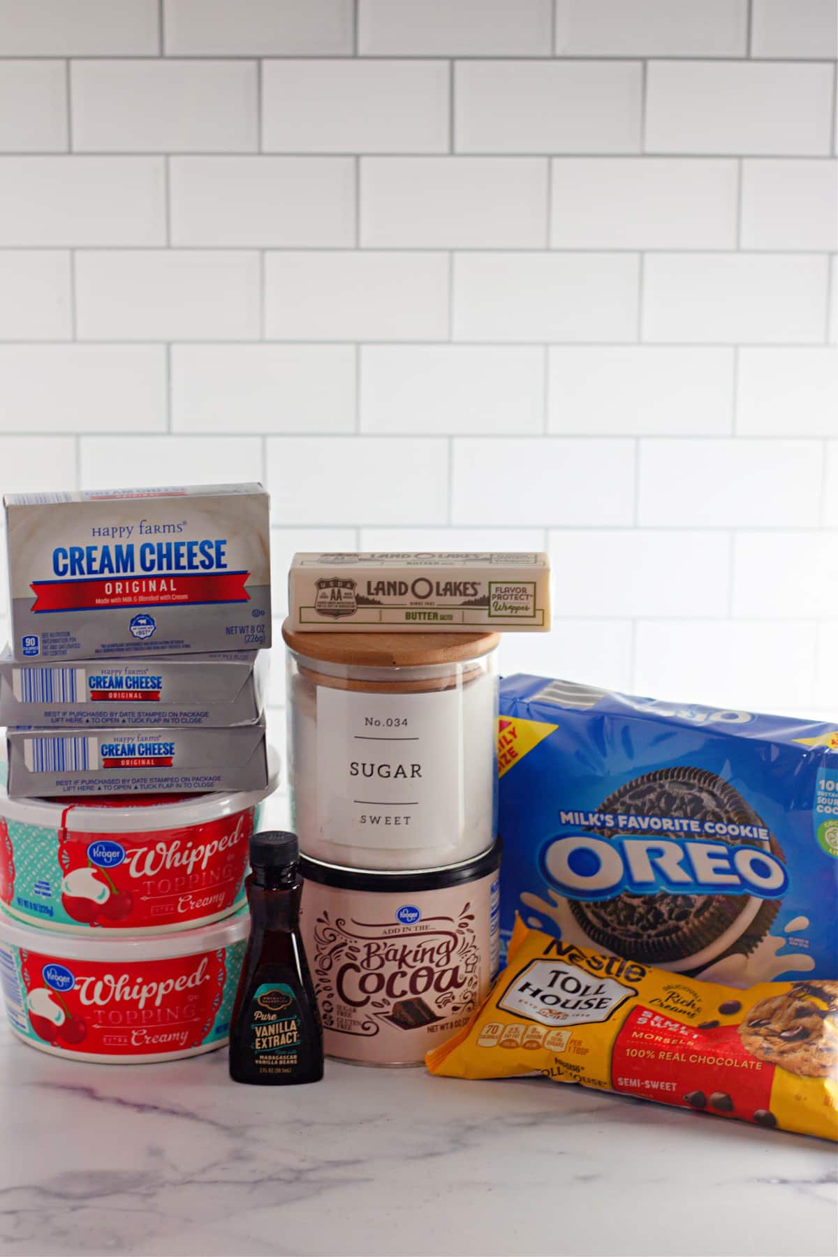 packages of cream cheese, whipped topping, butter, sugar, vanilla, cocoa, Oreo's and chocolate chips on a counter.