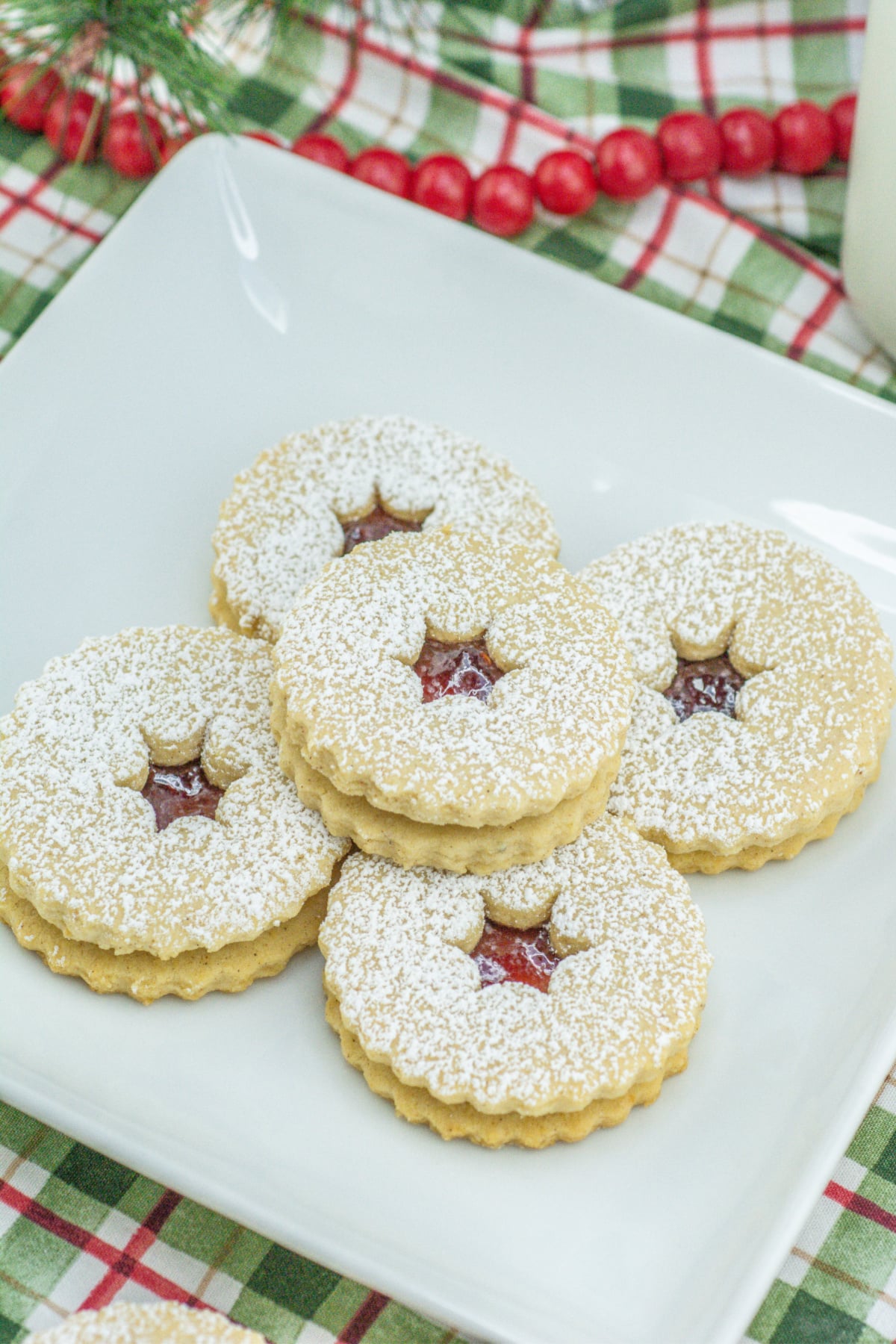 raspberry linzer cookies stacked on a plate.