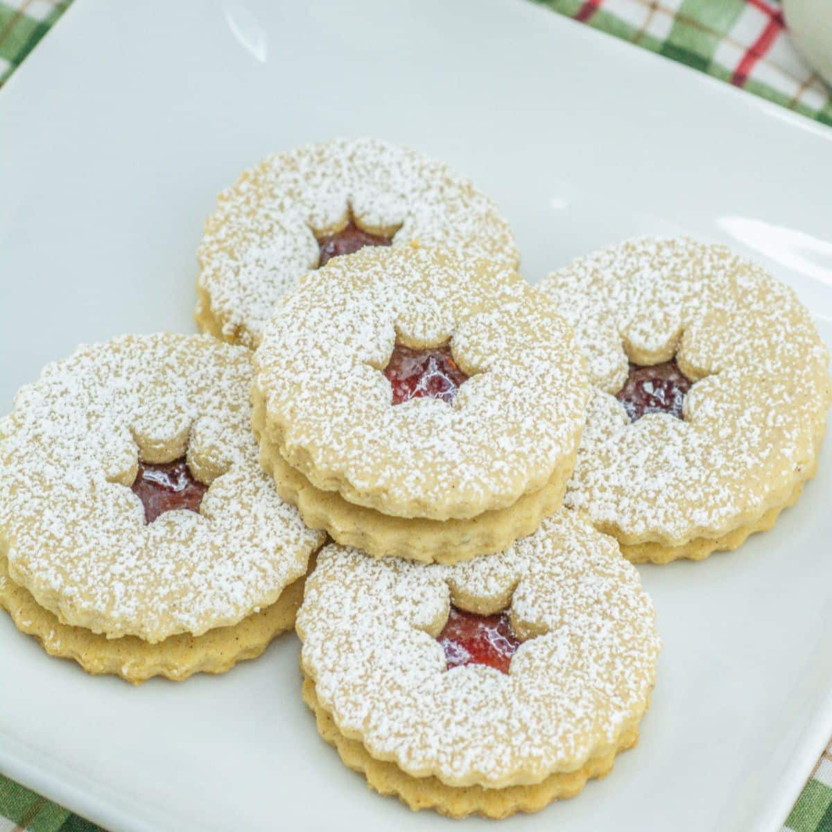 raspberry linzer cookies stacked on a plate.