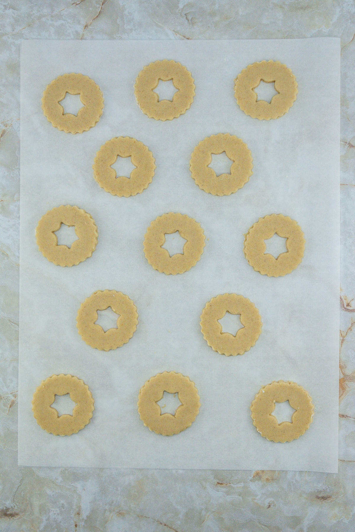raw linzer cookies being cut on a piece of parchment paper.