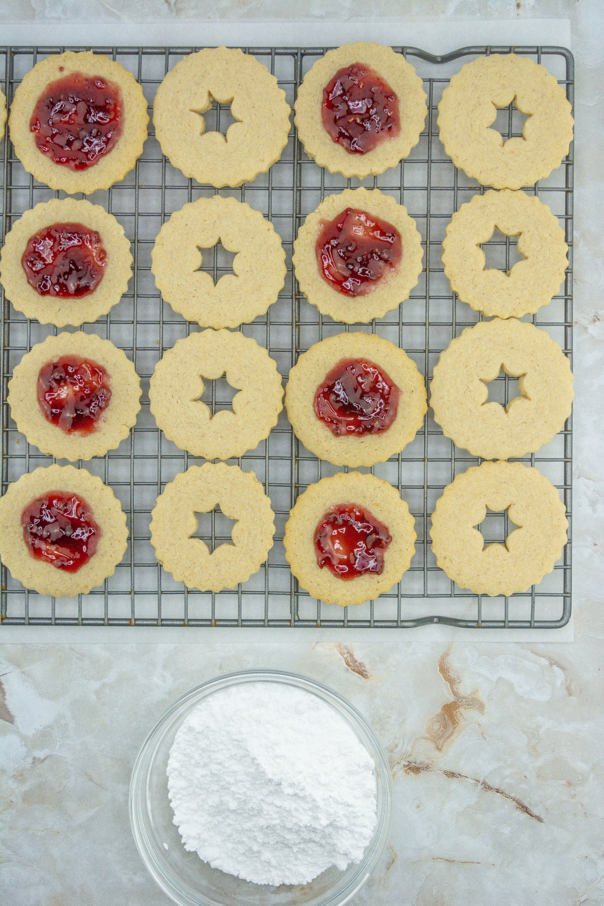 raspberry linzer cookies being filled in a wire cooling rack.