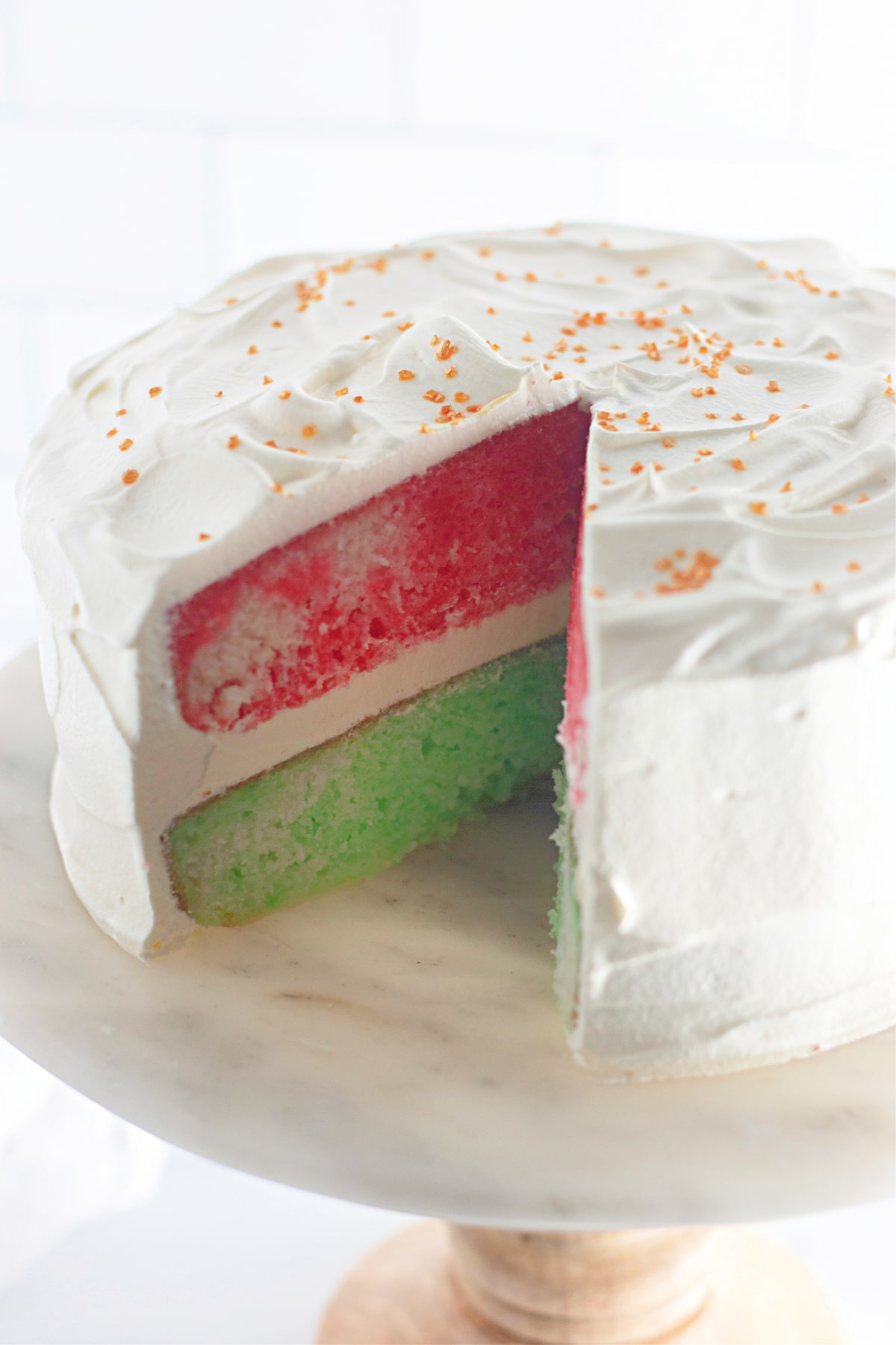 red and green christmas cake with a slice missing on a cake stand.