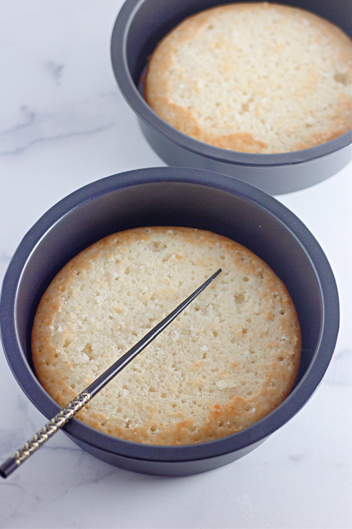 holes being poked into baked round cakes still in the pan with a chopstick.