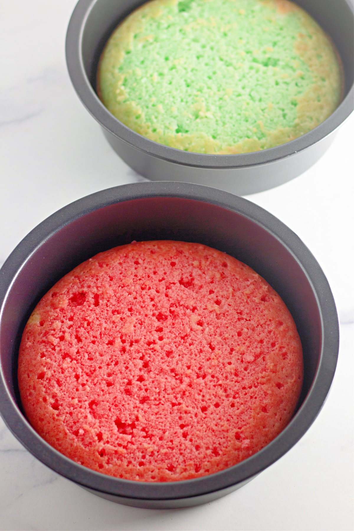two round cake pans filled with a baked cake layers that have been covered in red and green jello.