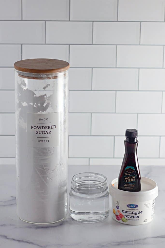 containers of powdered sugar, water, meringue powder, and vanilla extract on a counter for royal icing.