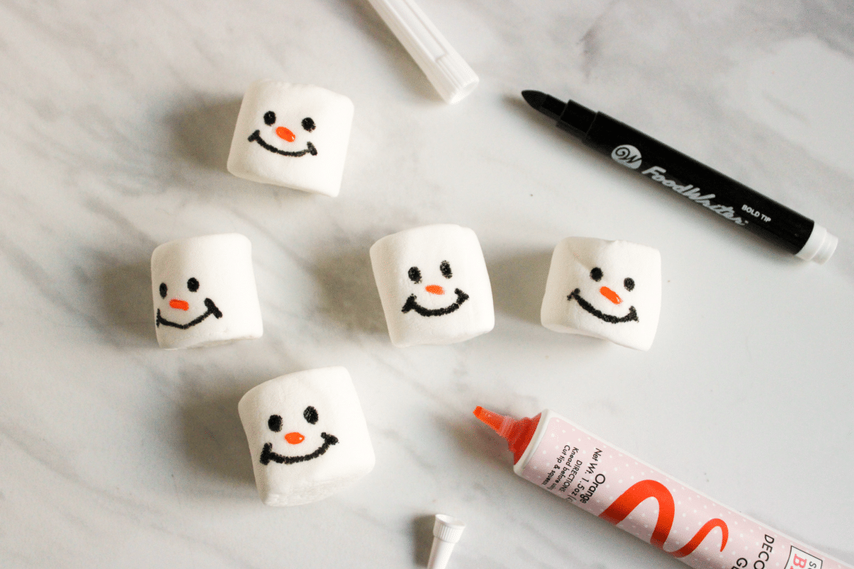 marshmallows with snowman faces being drawn onto them.