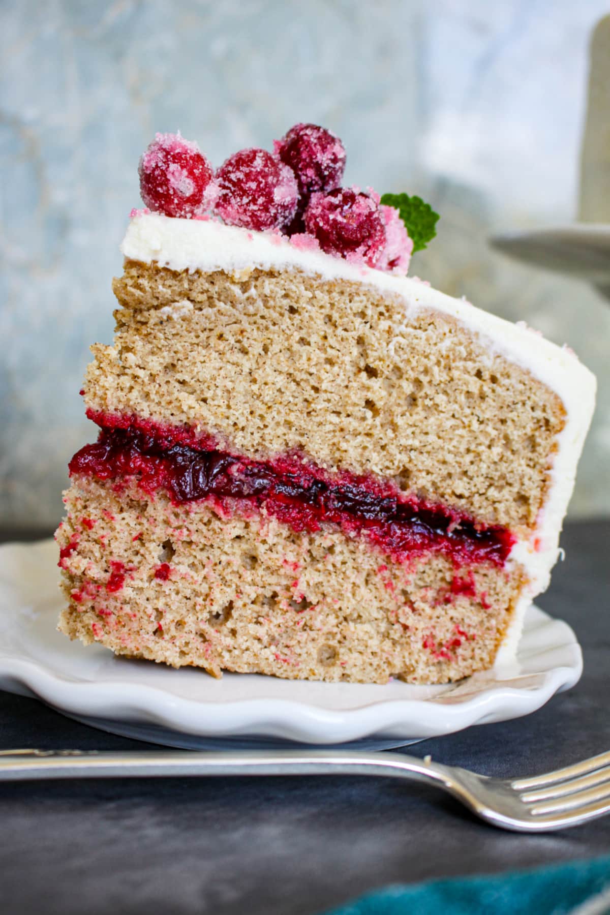 slice of spice cake with cranberry filling topped with sugared cranberries on a plate.
