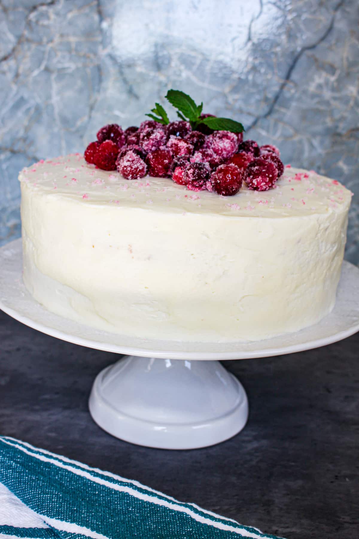 uncut spice cake with cranberry filling topped with sugared cranberries on a cake stand.