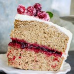 slice of spice cake with cranberry filling topped with sugared cranberries on a plate.