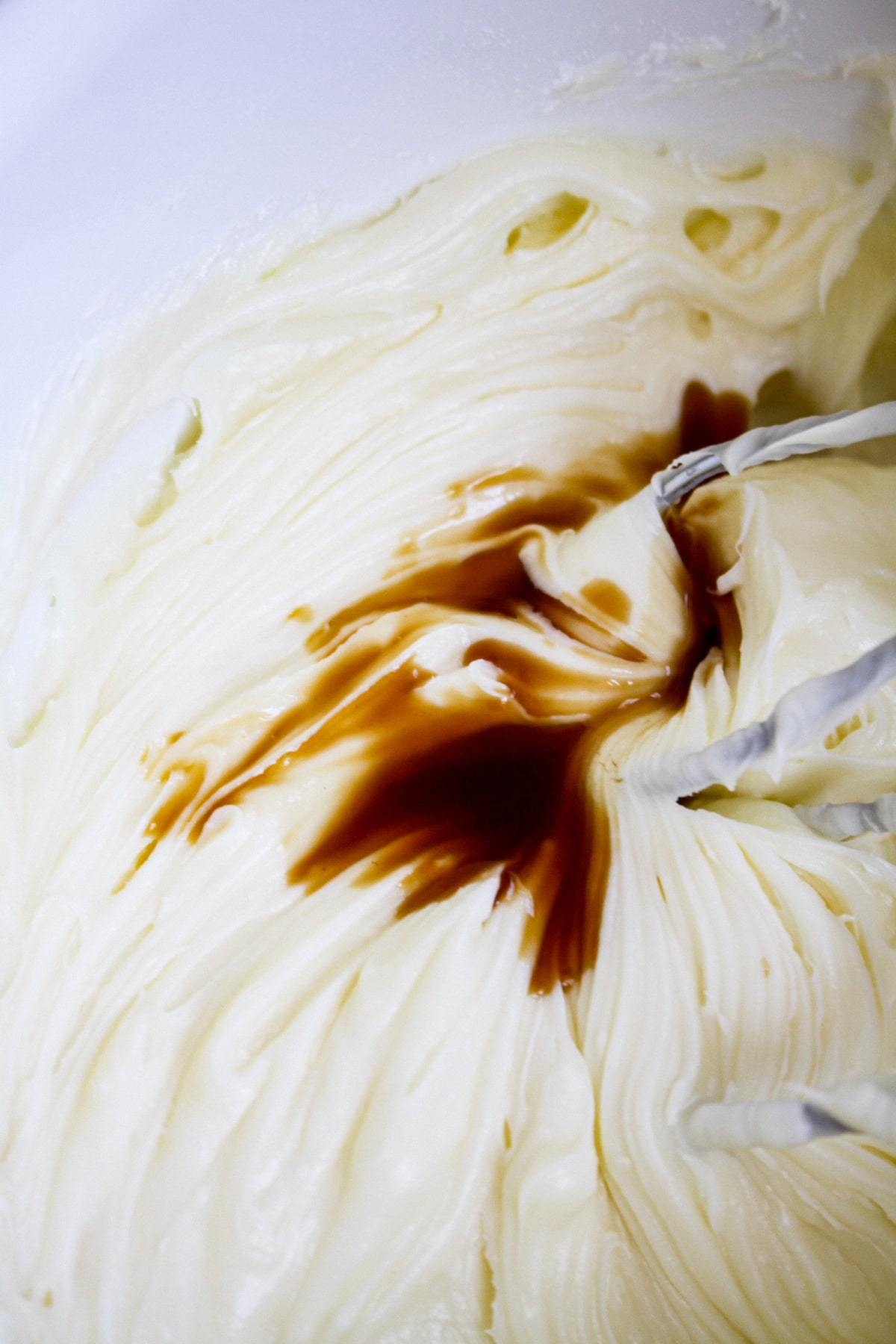 vanilla extract being added to a cream cheese frosting in a mixing bowl.