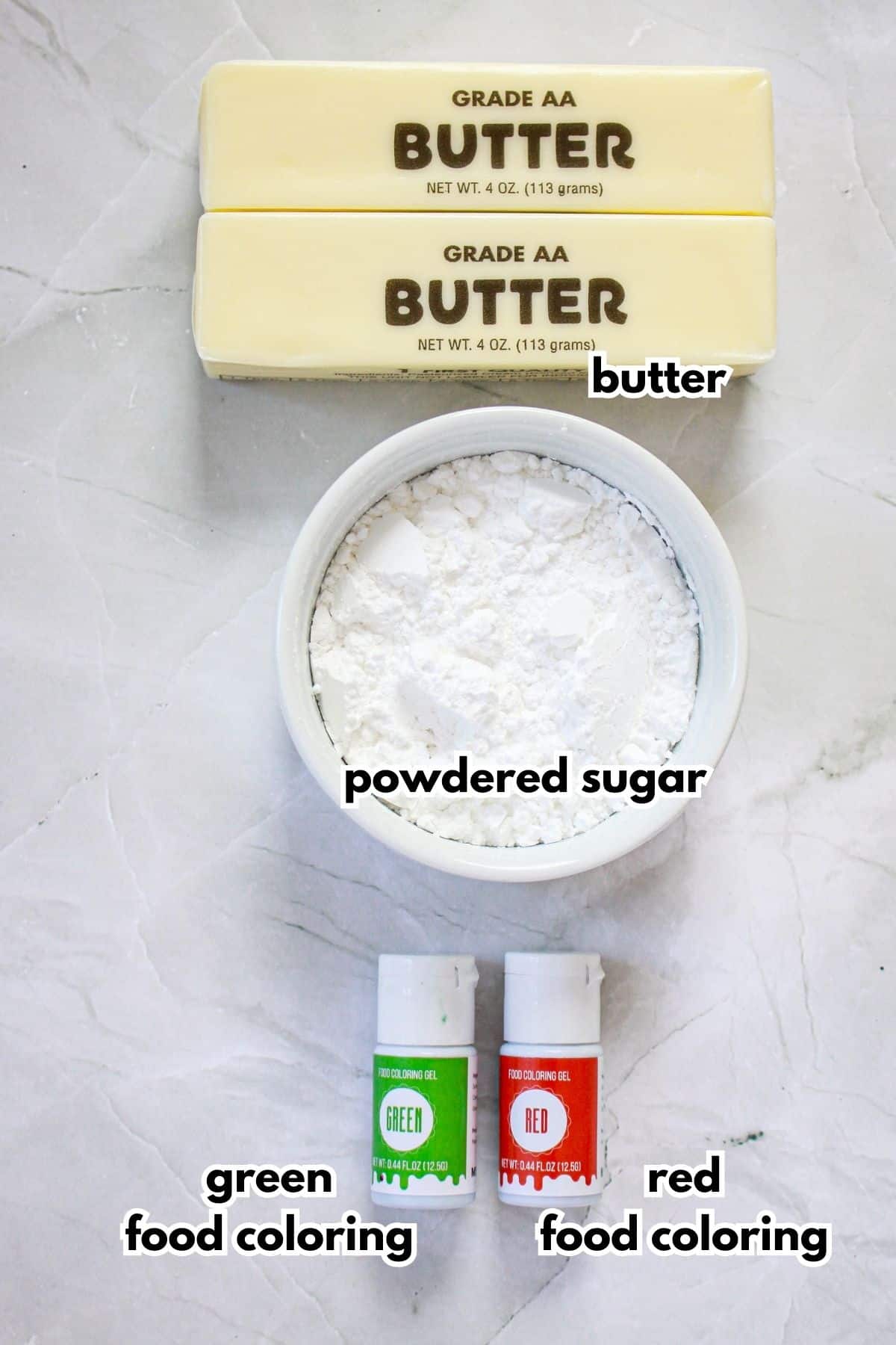 two sticks of butter, bowl of powdered sugar, and bottles of red and green food coloring.