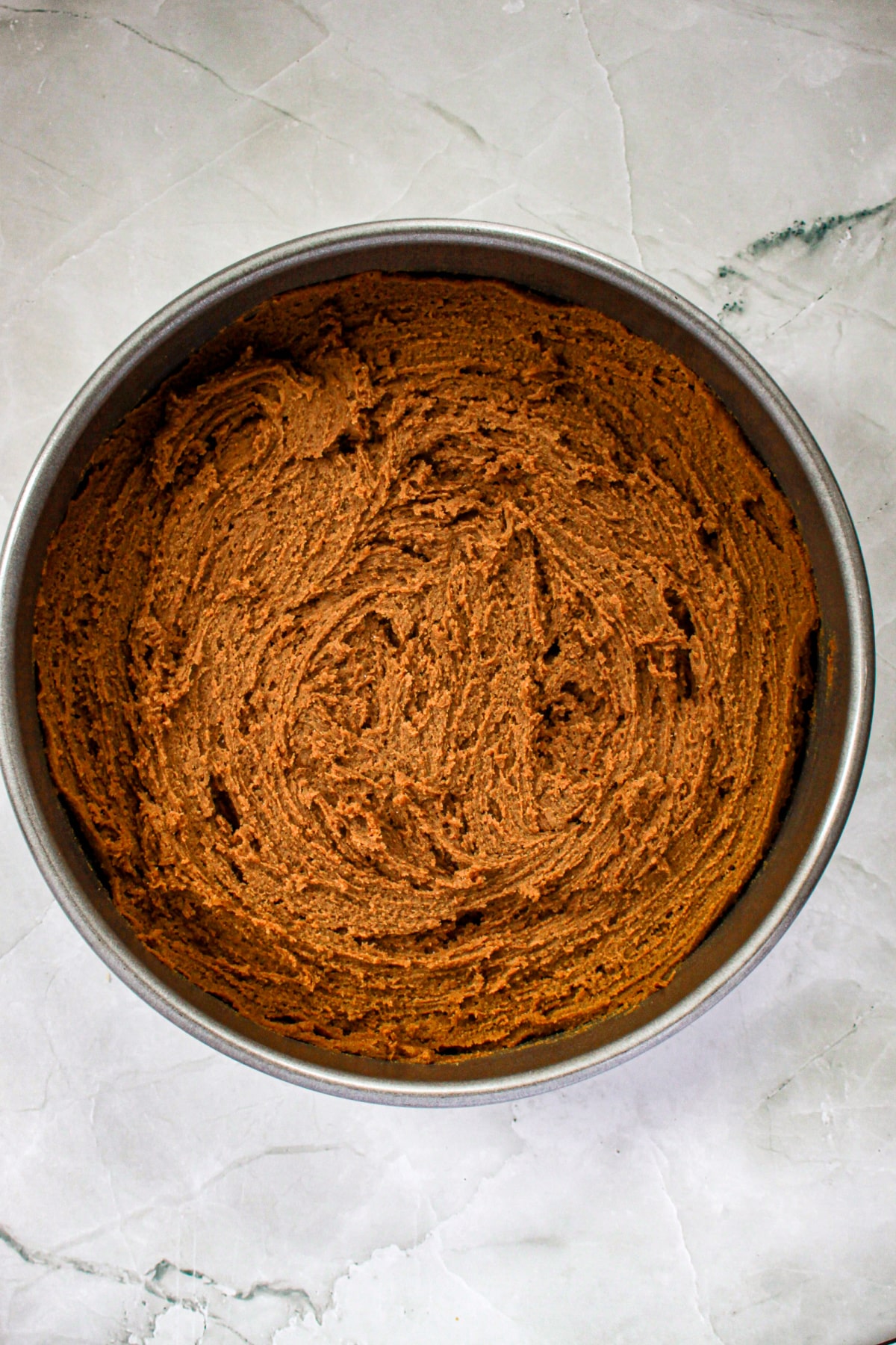 spice cookie dough being spread into a round cake pan.