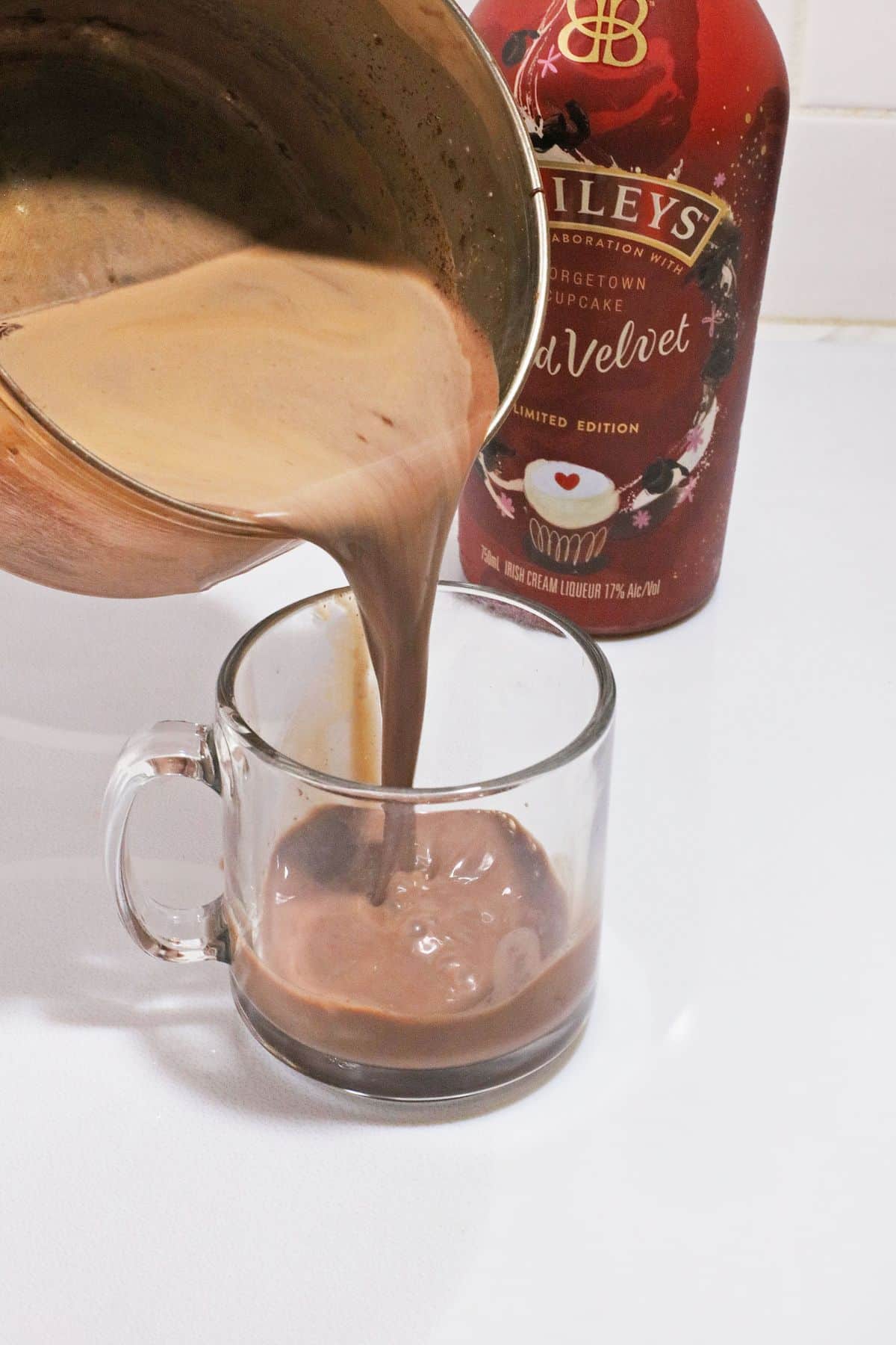 hot cocoa being poured into a glass mug.