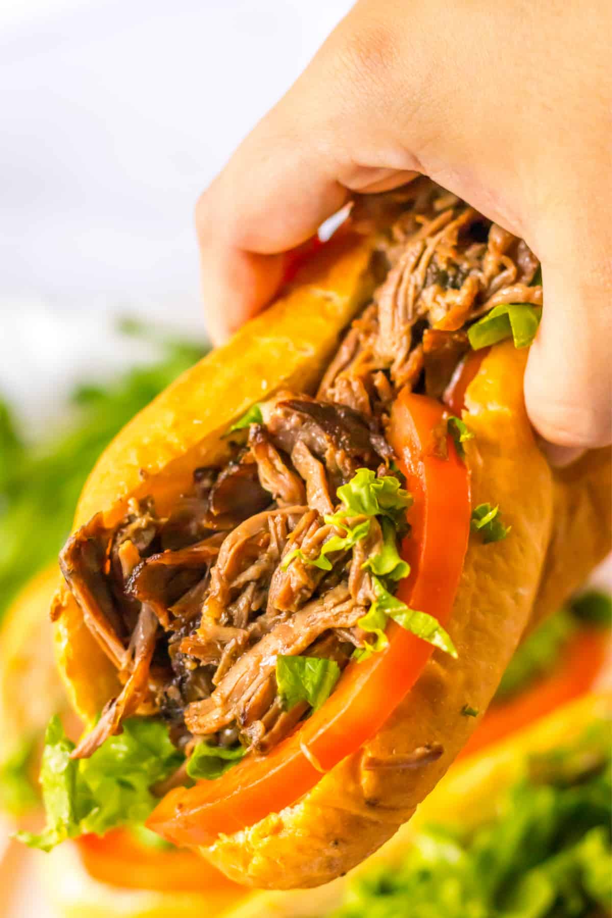 slow cooker beef po boy held in a woman's hand in the air.