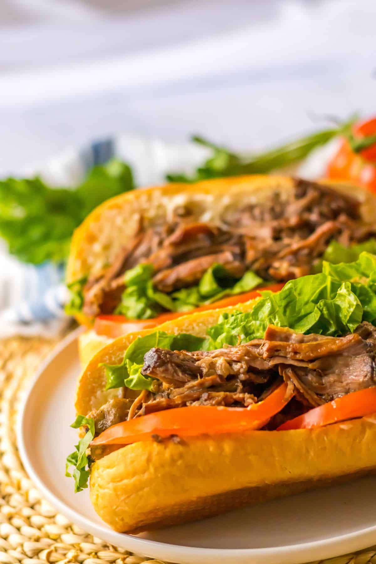 two slow cooker beef po boy sandwiches on a plate.