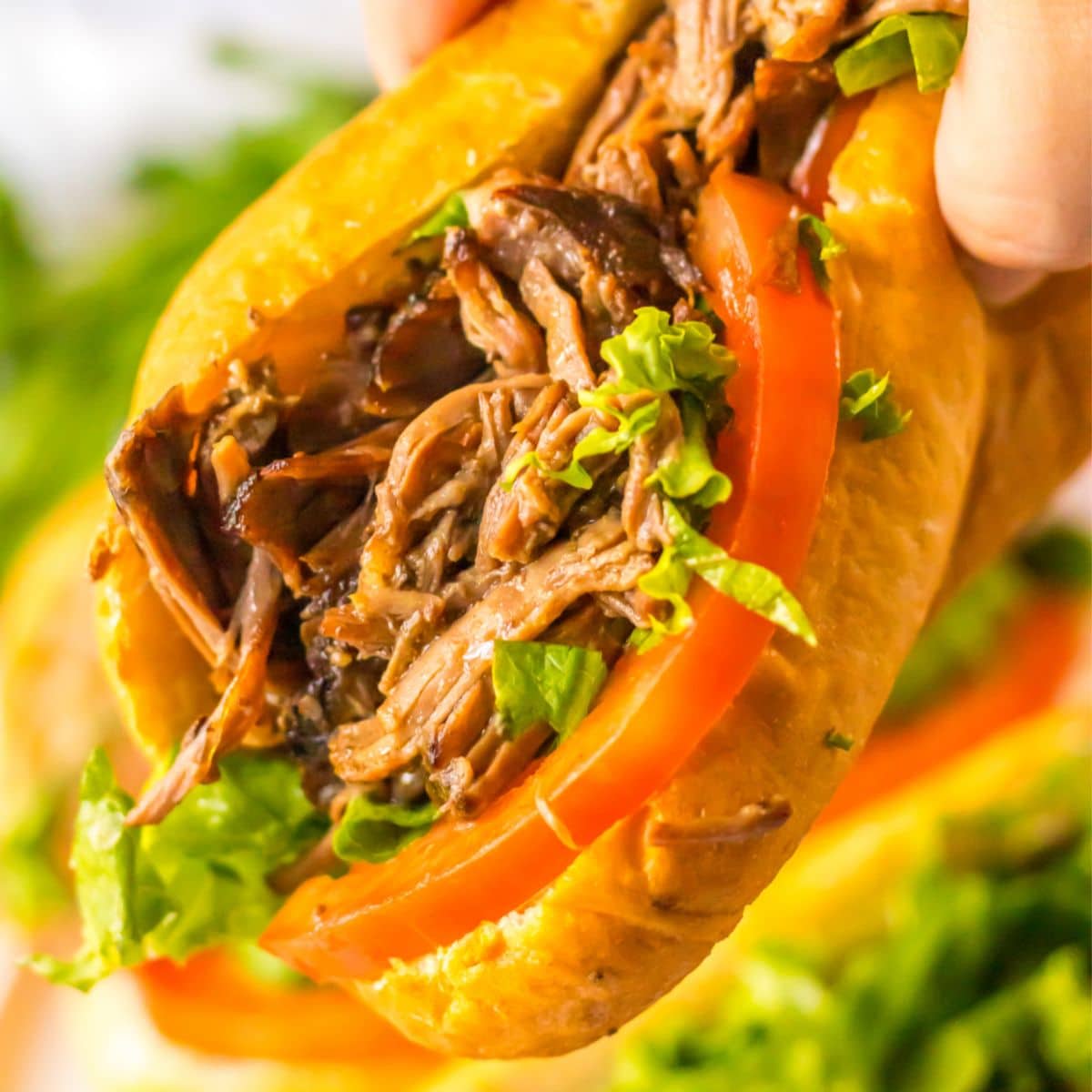 slow cooker beef po boy held in a woman's hand in the air.