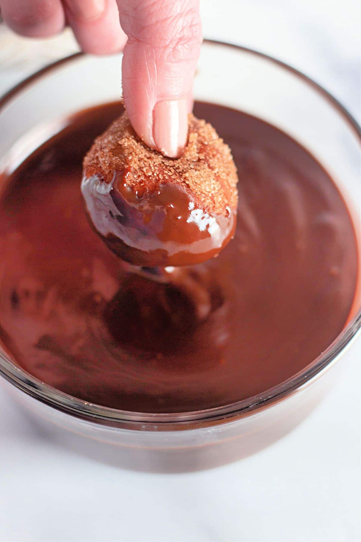 biscuit donut hole held in a woman's fingers being dipped into chocolate sauce.