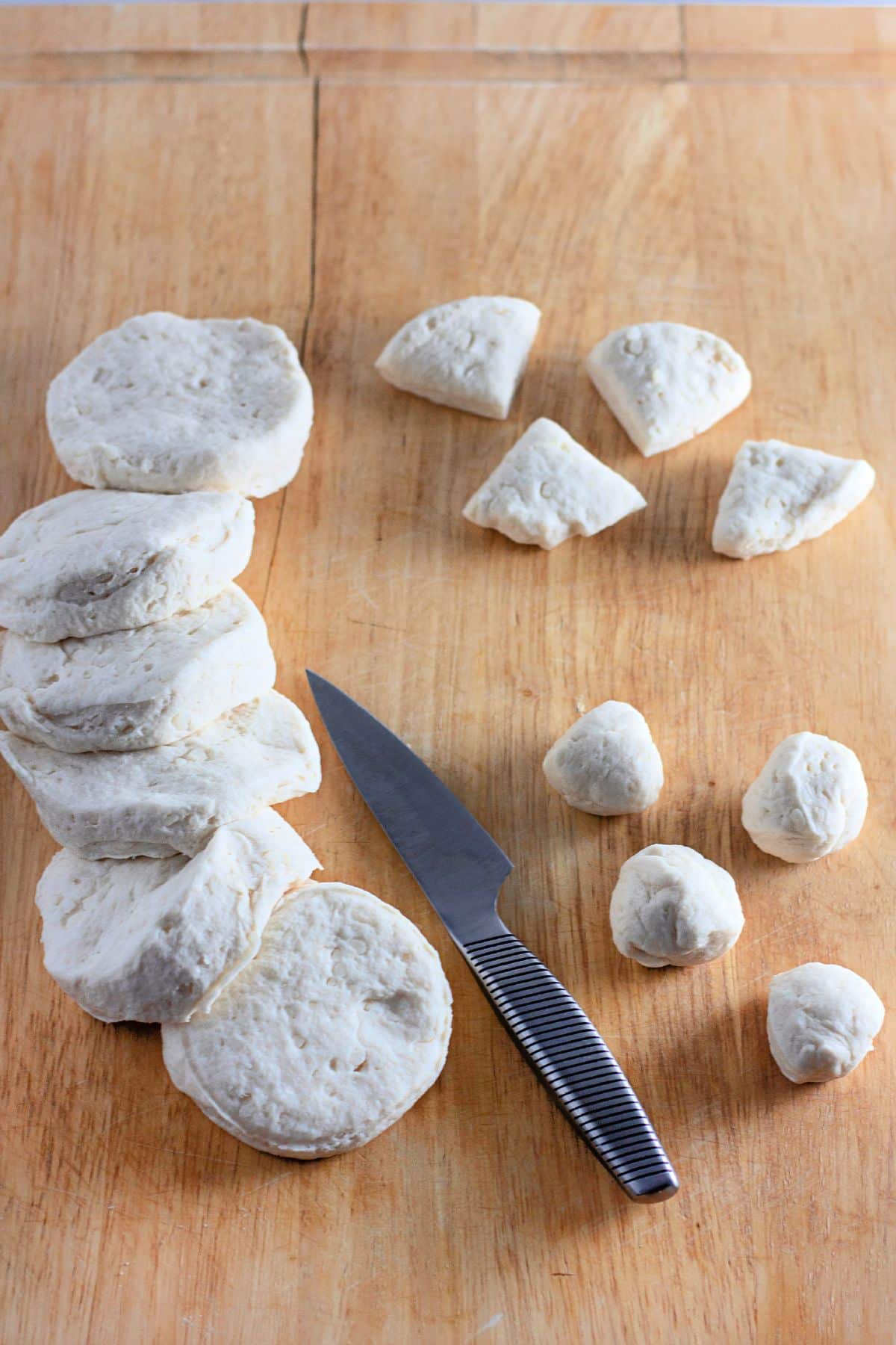 canned biscuit dough being cut into quarters and rolled into balls on a cutting board.