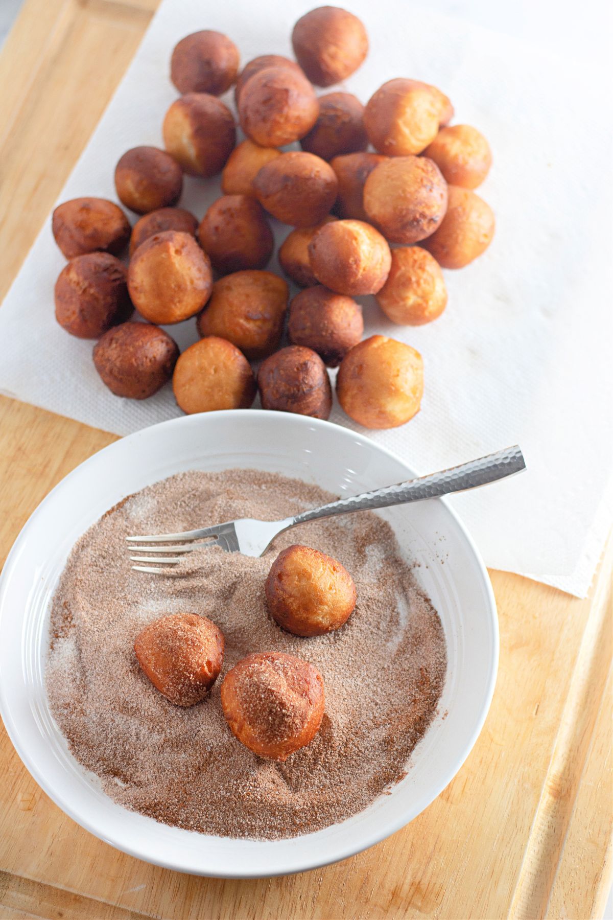 three donut holes being coated in cinnamon sugar on a small plate.