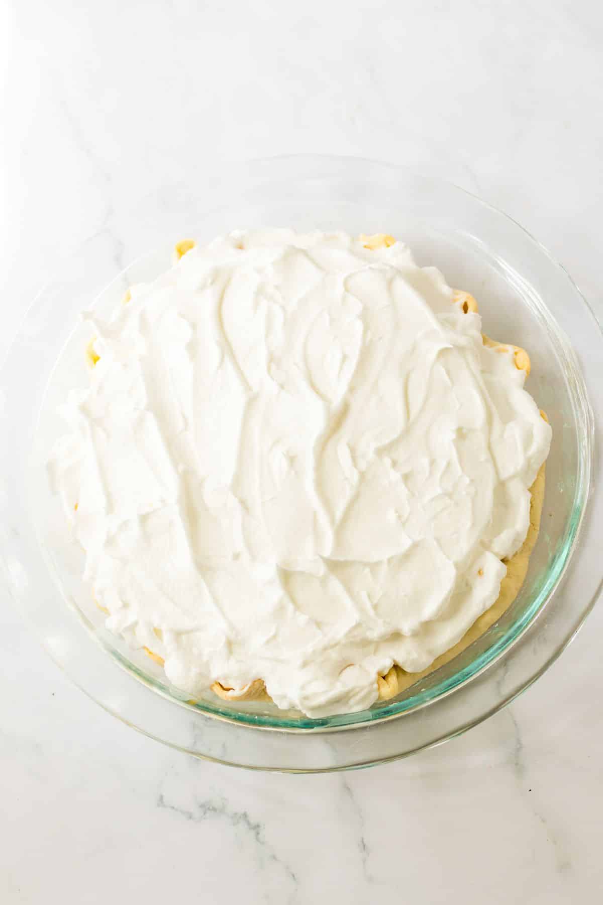 meringue being added on top of a butterscotch pie.