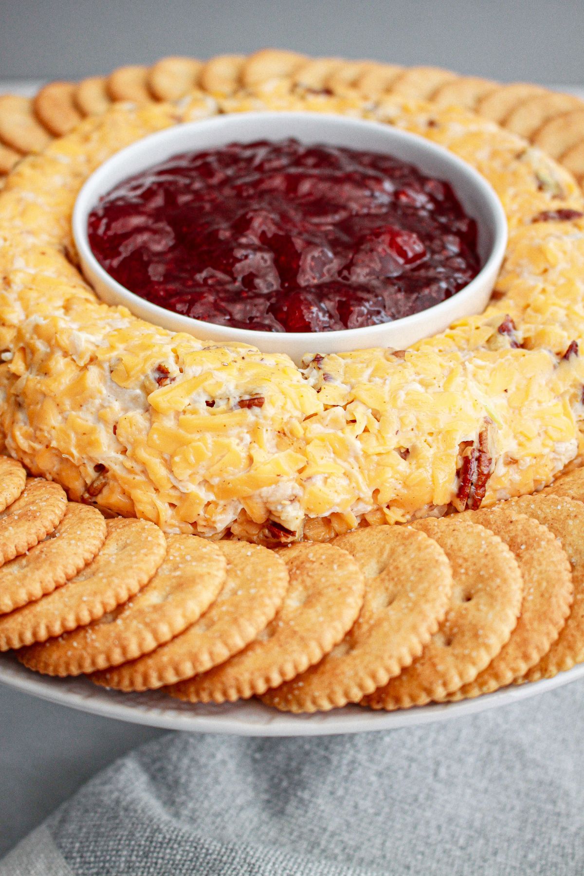 cheese ring on a platter with jam in the center and crackers on the outside.