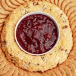 cheese ring on a platter with jam in the center and crackers on the outside.