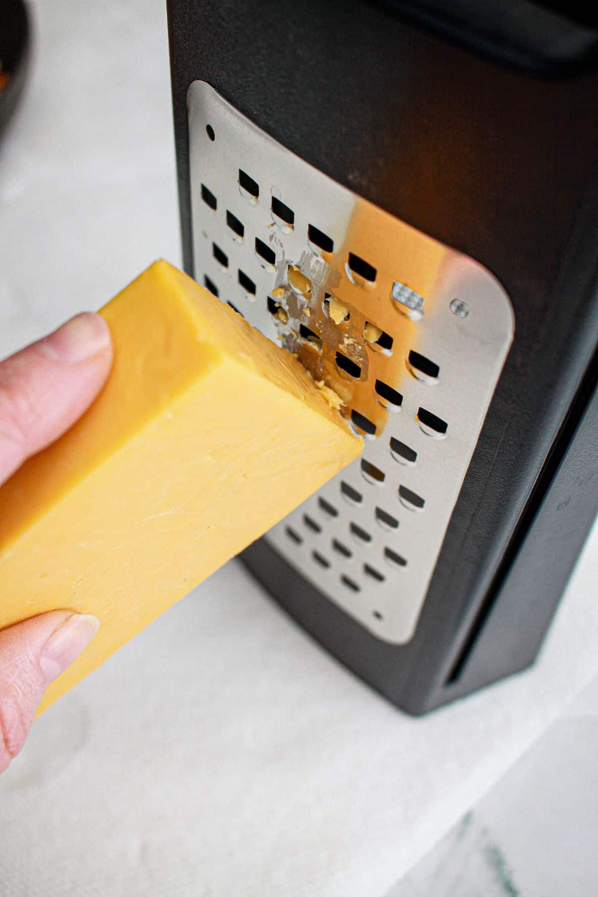 block of cheddar cheese being grated on a box grater.
