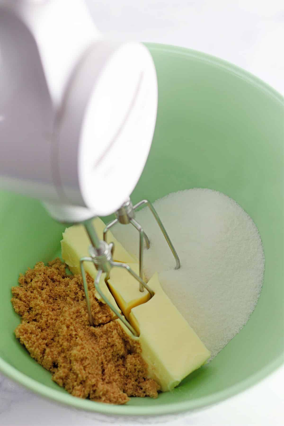 butter and sugar being creamed with a hand mixer in a mixing bowl.
