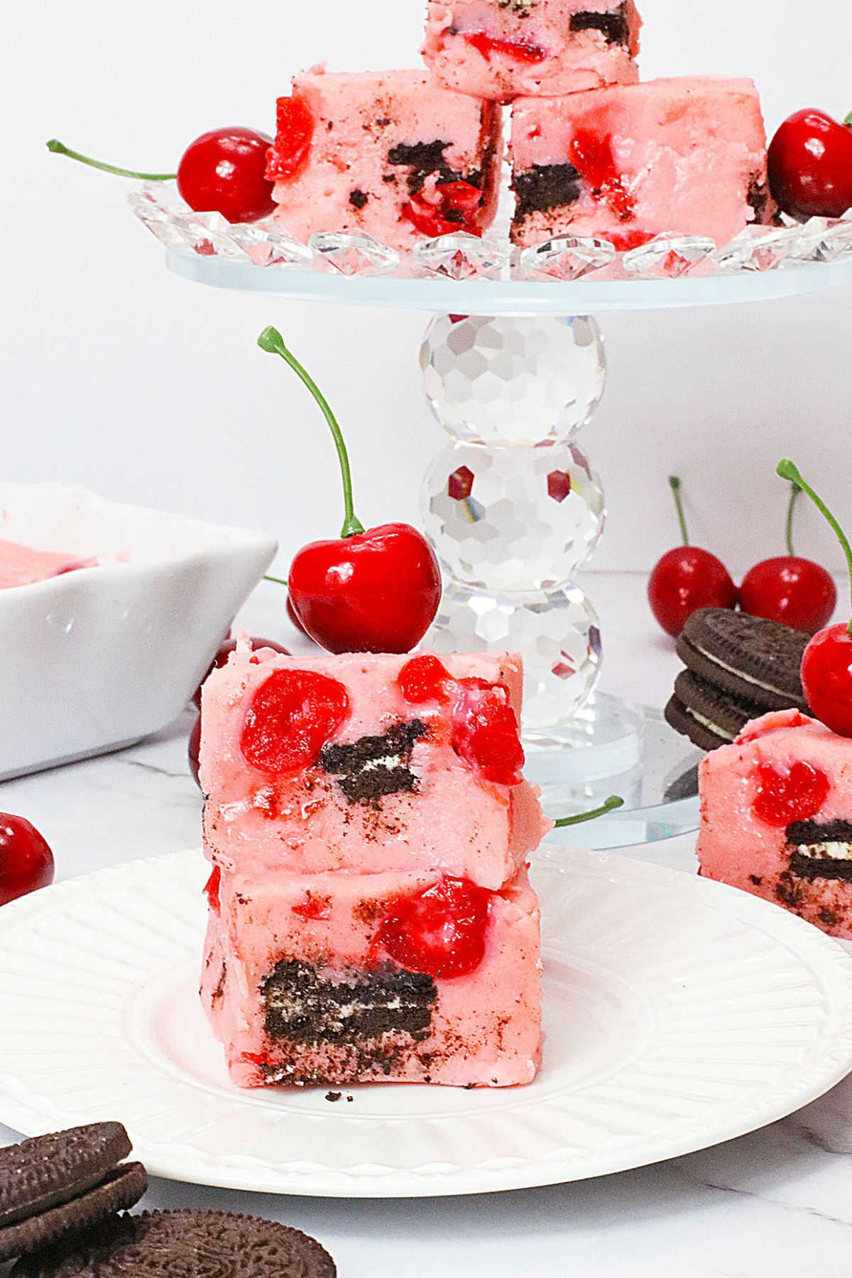 two slices on chocolate cherry fudge on a plate topped with a fresh cherry.