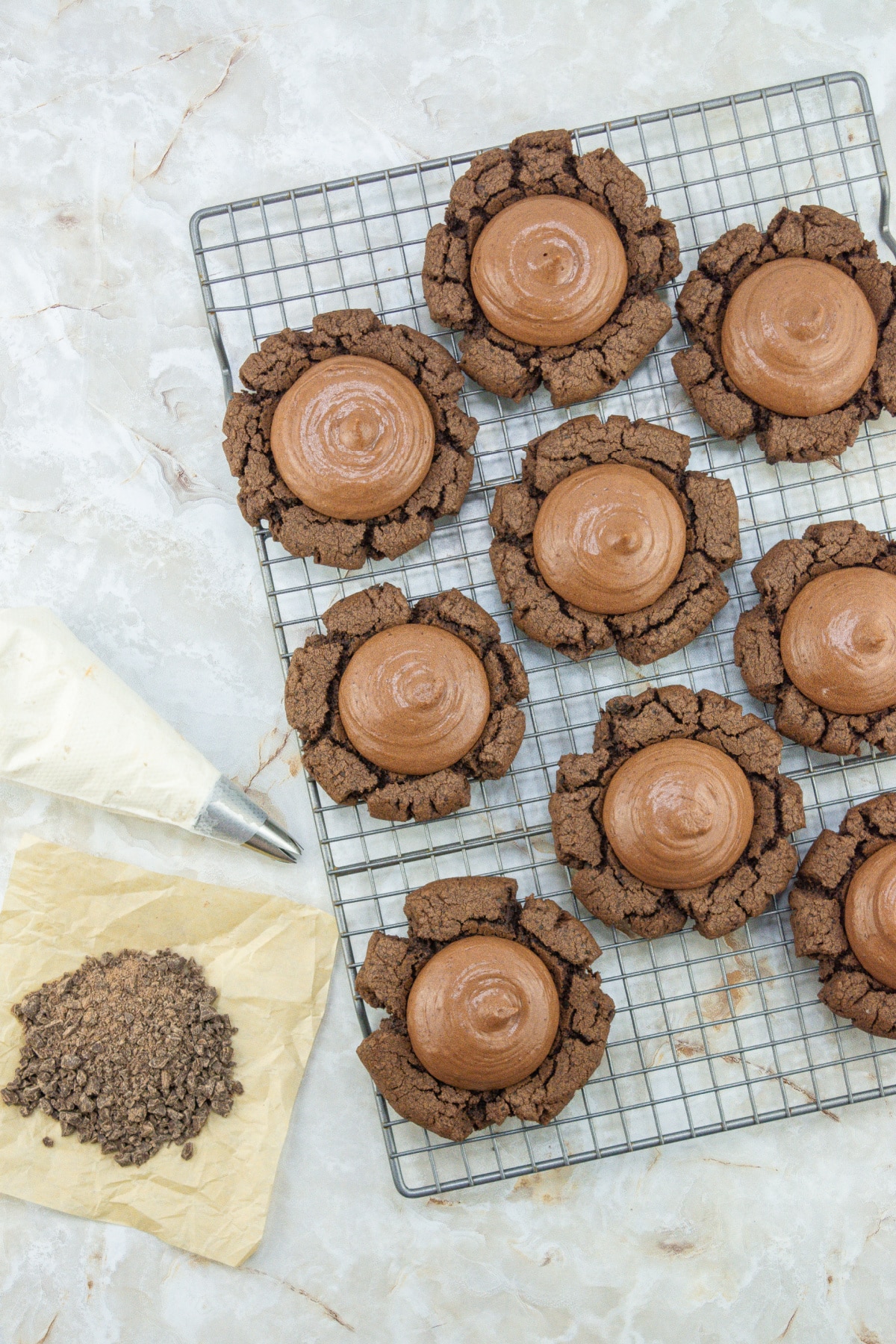 chocolate filling being piped on top of cookies on a wire rack.