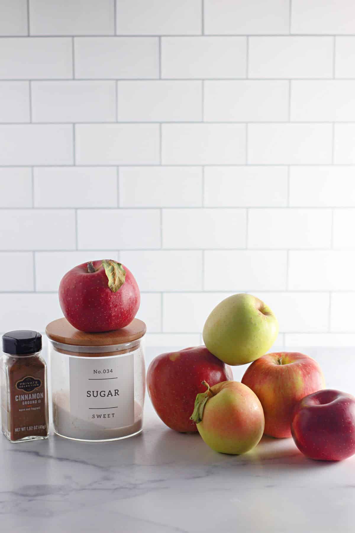 apples, canister of sugar, and a jar of cinnamon on a counter.