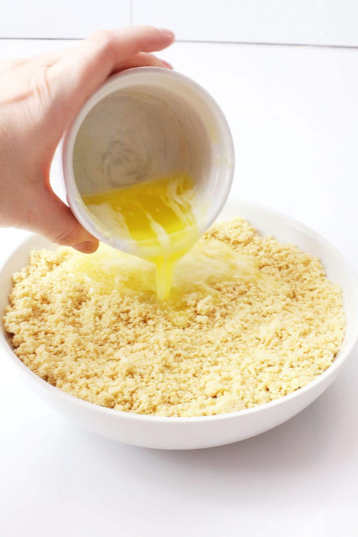 melted butter being added to a bowl full of crushed golden oreo cookies.