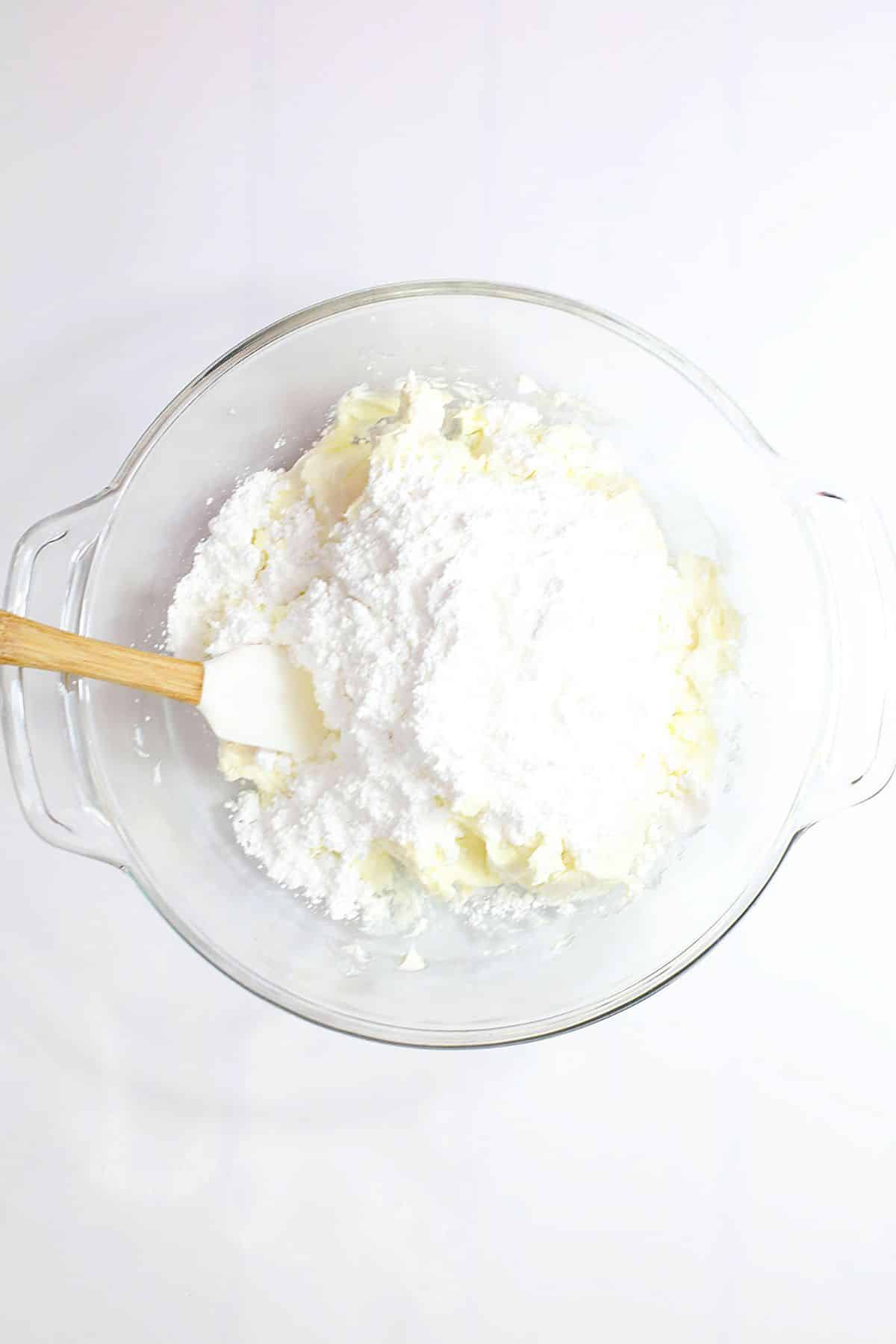 cream cheese and powdered sugar being mixed together in a glass bowl.