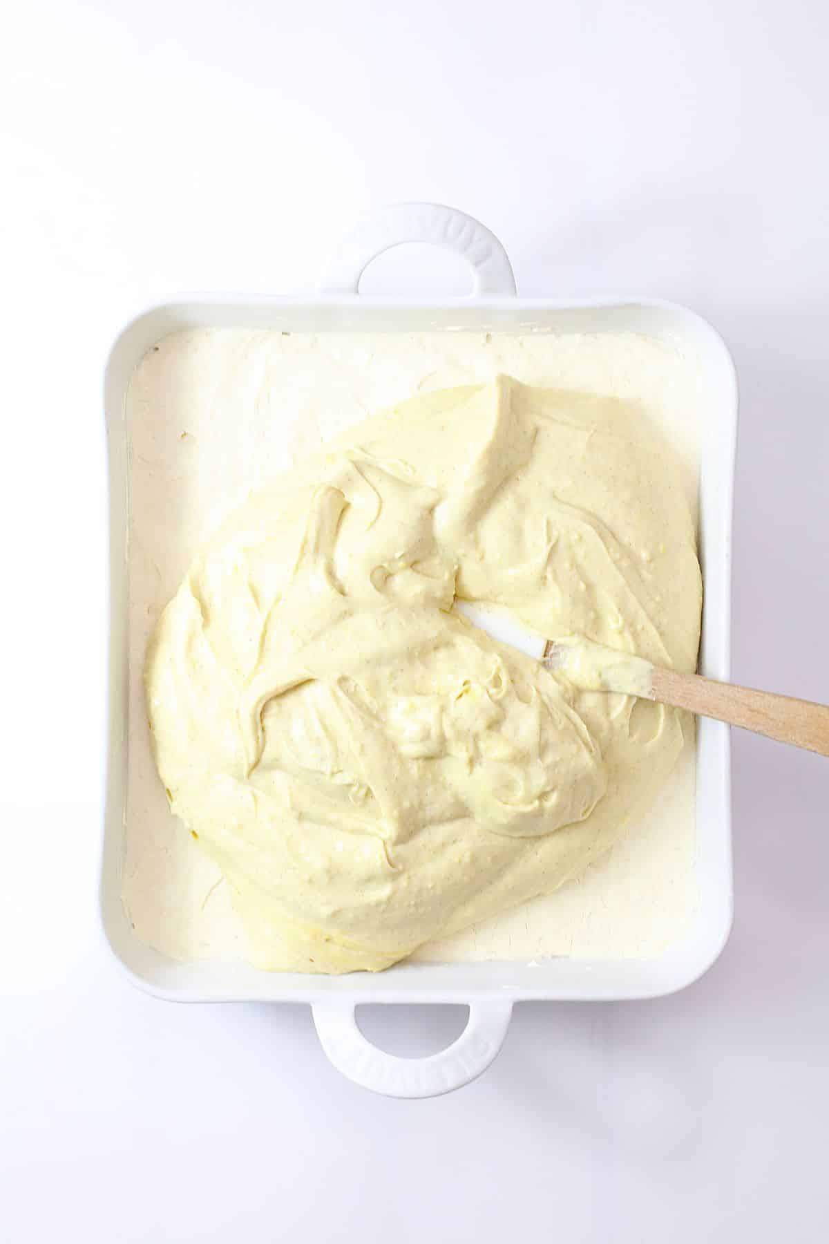 vanilla pudding layer being spread on top of the cream cheese layer in a baking dish.