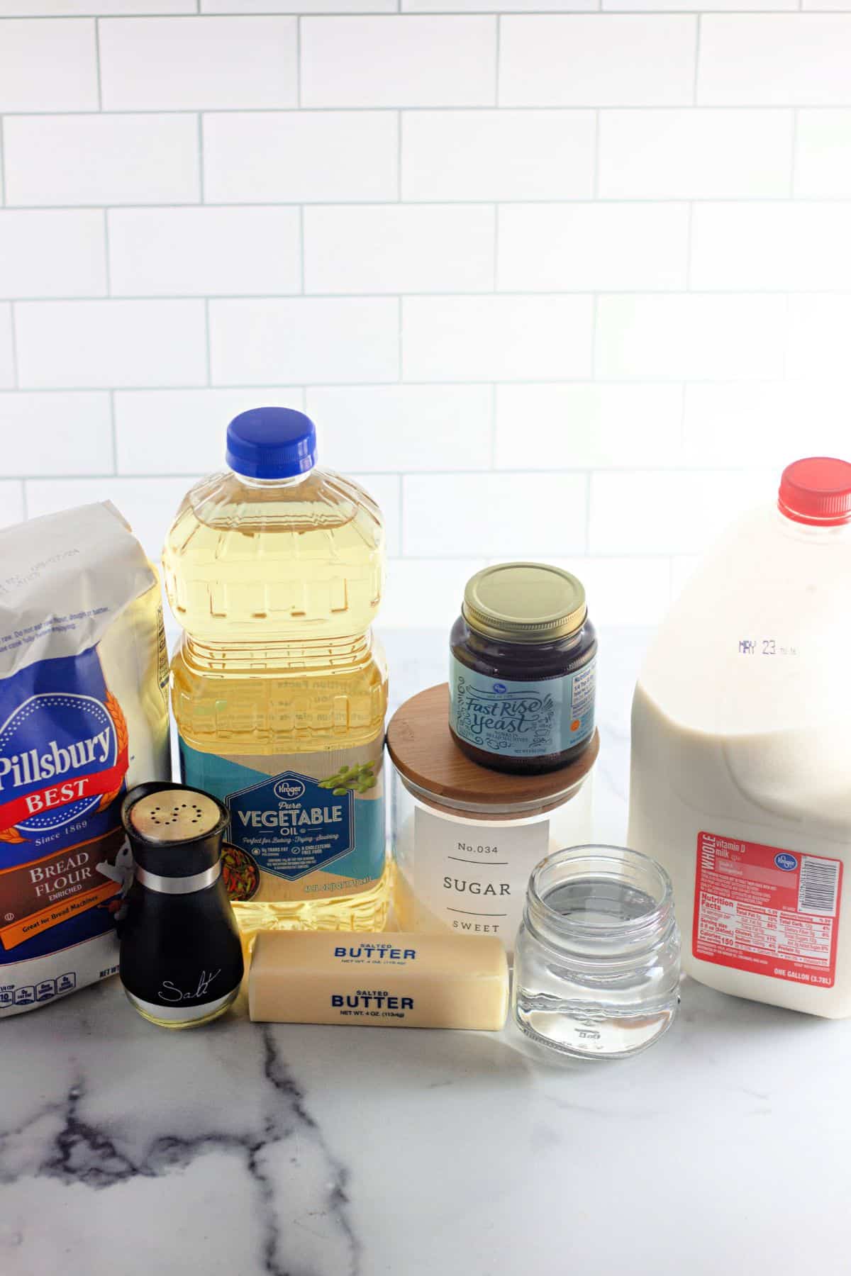 flour, oil, salt, butter, sugar, yeast, water and milk on a counter.