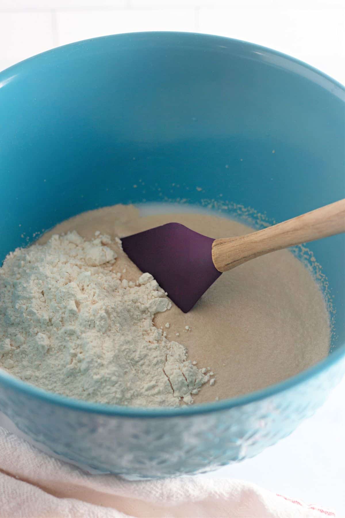 flour being added to bloomed yeast in a mixing bowl.