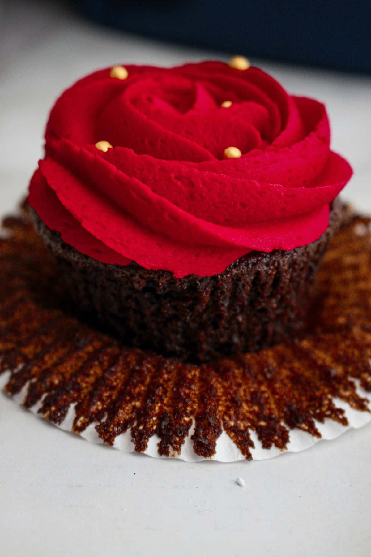 unwrapped devils food cupcake with a red rose piped on top.