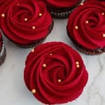 devils food cupcakes on a marble counter with a red rose piped in frosting on the top.